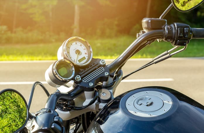 Cruscotto e manubrio di una moto Harley-Davidson con tachimetro analogico e display digitale, serbatoio nero lucido, su strada assolata.