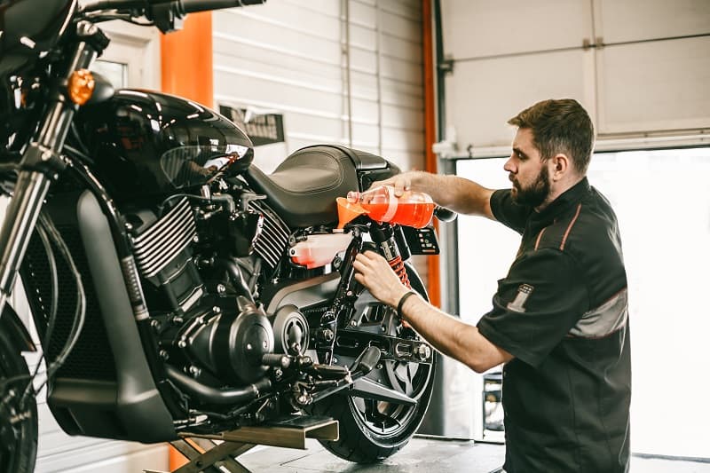 Tecnico specializzato Harley-Davidson esegue manutenzione, rabboccando il liquido di raffreddamento in una moto nera su sollevatore in officina.