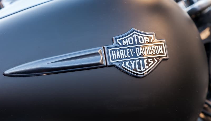 Serbatoio nero opaco di una moto Harley-Davidson con l'iconico logo Bar & Shield cromato. Rappresenta lo stile dei nostri motori.