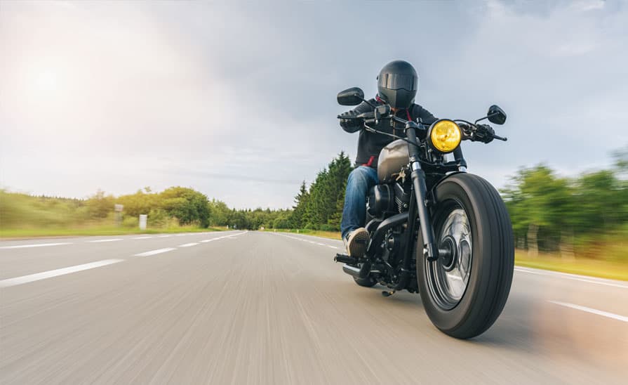 Motociclista con casco alla guida di una moto Harley-Davidson su strada, con effetto mosso che enfatizza la dinamicità e la velocità.