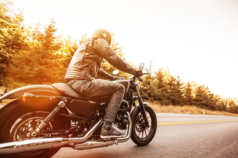 Rider con abbigliamento tecnico su moto Harley-Davidson in test ride su strada panoramica. Esperienza di guida e motori.