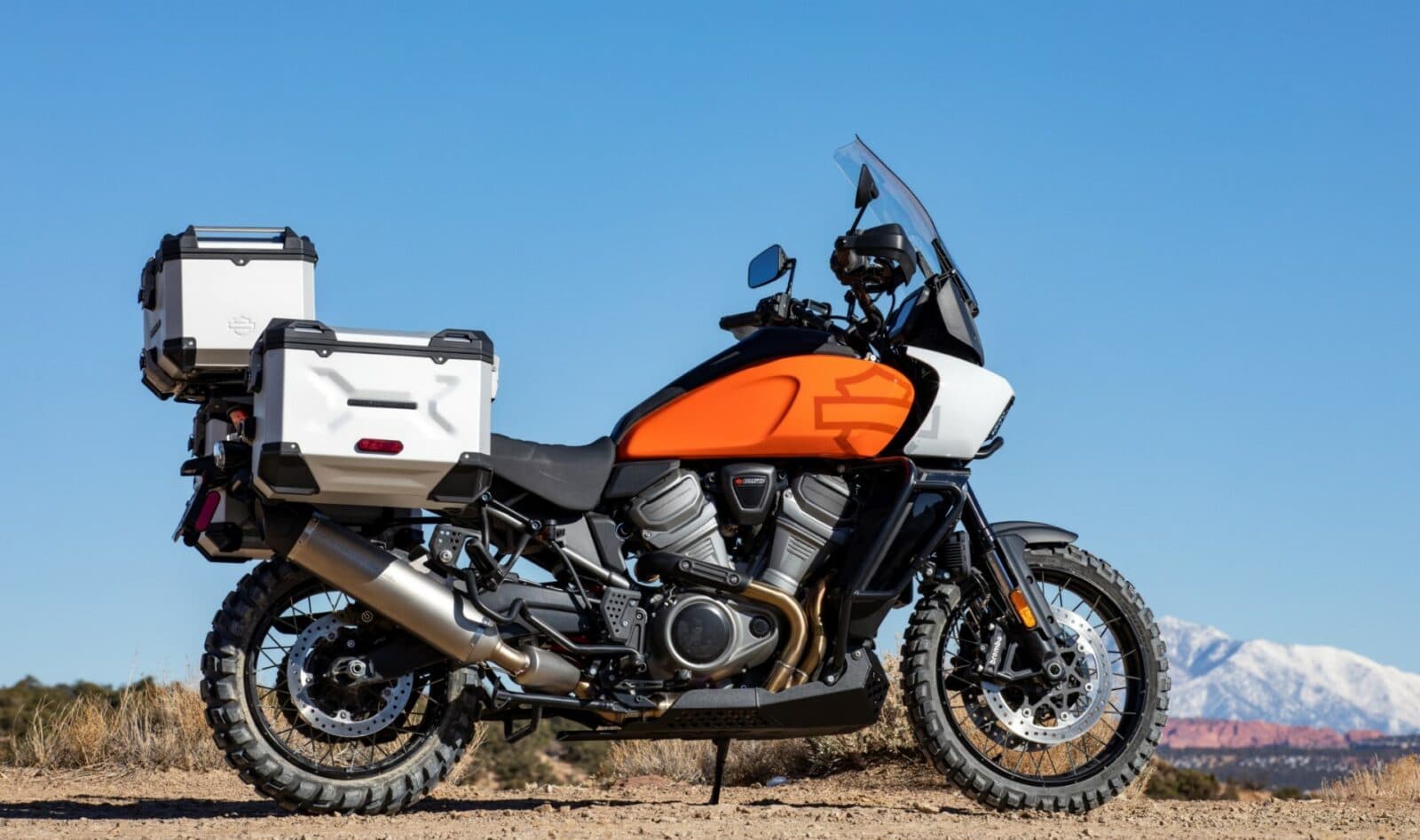 Harley-Davidson Pan America 1250 Special, moto adventure touring arancione e bianca, con borse laterali e top case, parcheggiata all'aperto. Ideale per test ride.
