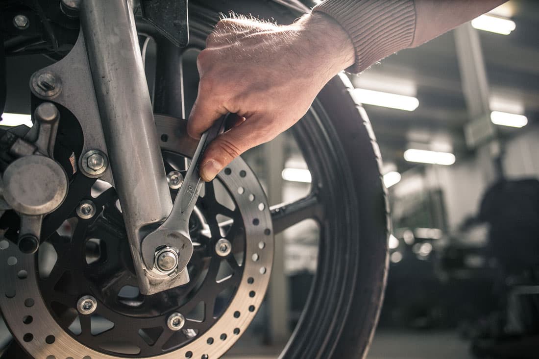 Mano di un meccanico che stringe un bullone sulla forcella anteriore di una moto con una chiave. Manutenzione professionale e cura dei motori.