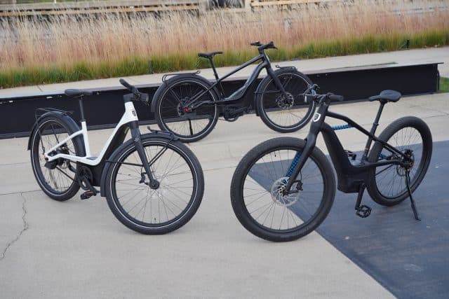 Tre e-bike Serial 1 di Harley-Davidson: un modello step-through bianco, uno urbano nero e uno sportivo nero, con freni a disco.