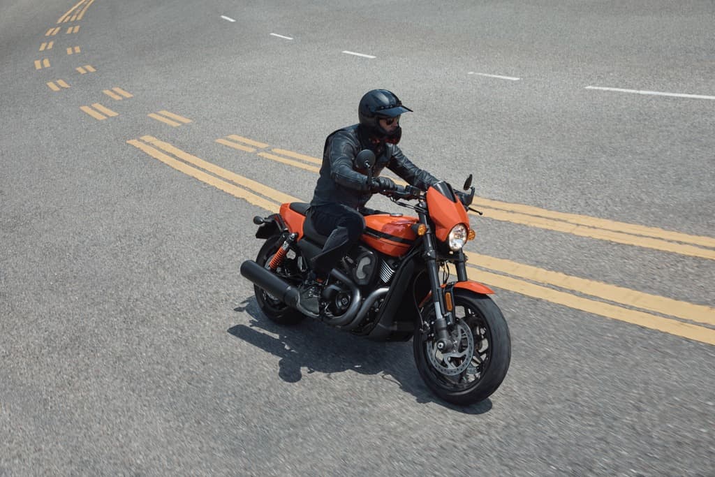 Motociclista con casco e giacca in pelle su moto Harley-Davidson arancione in movimento su strada asfaltata. Perfetta per un test ride.