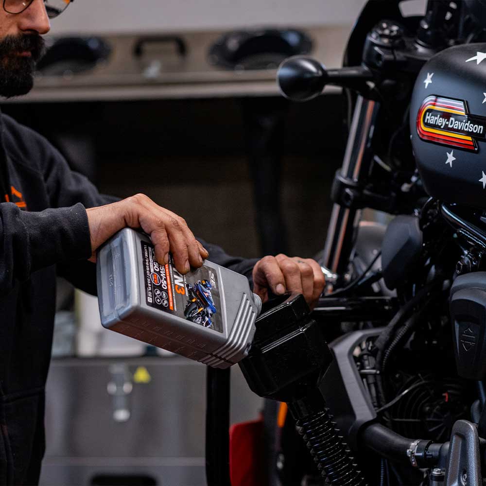 Meccanico versa olio motore 5W-50 N3 in una moto Harley-Davidson, evidenziando la manutenzione del motore.
