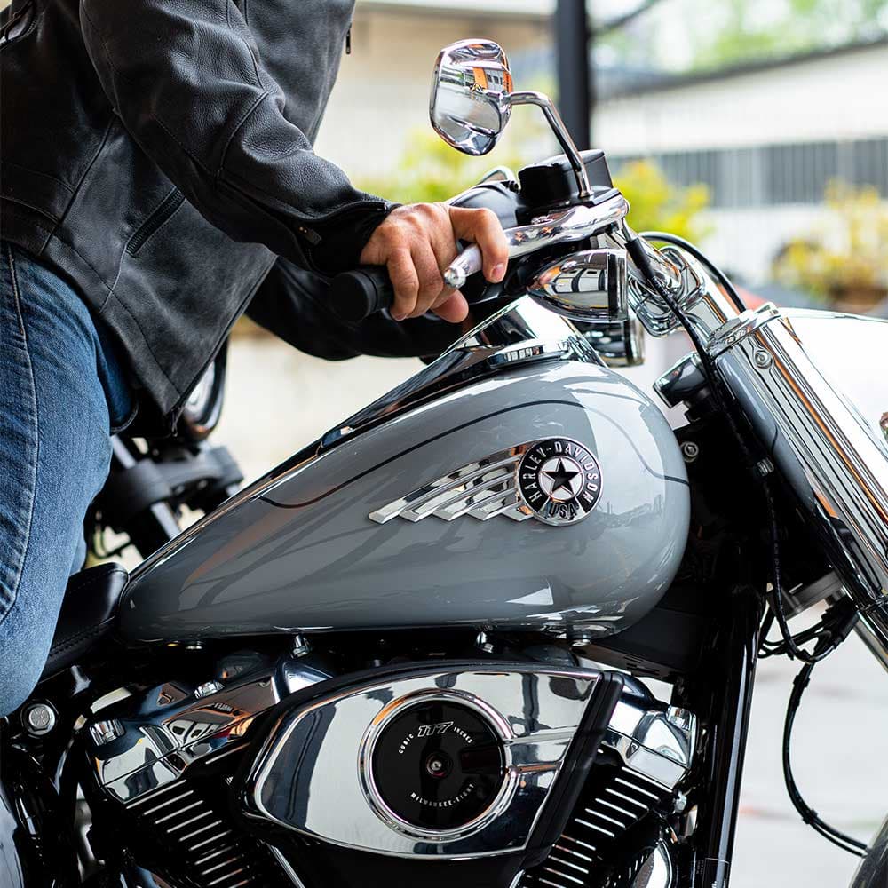 Motociclista con abbigliamento in pelle su Harley-Davidson grigia. Dettaglio serbatoio con logo e motore Milwaukee-Eight 117. Pronta per test ride.