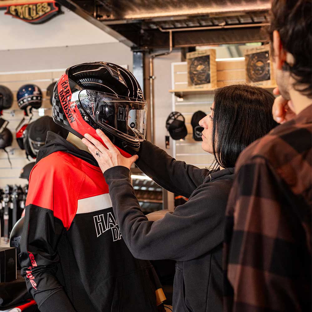 Donna sistema un casco integrale Harley-Davidson su manichino con felpa, in concessionaria. Esposizione abbigliamento e accessori moto.