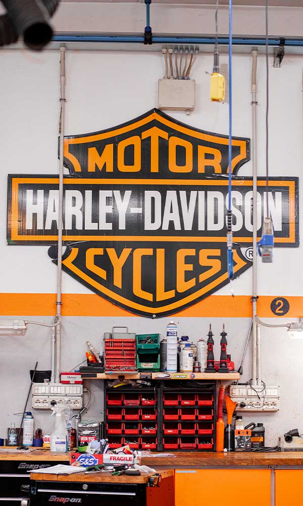 Officina Harley-Davidson con grande logo, banco da lavoro professionale e organizzazione ricambi, per assistenza qualificata a moto e motori.