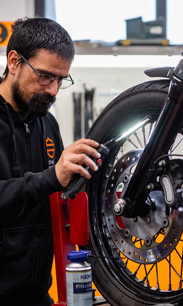 Meccanico specializzato ispeziona il pneumatico anteriore e il freno a disco di una moto Harley-Davidson con luce da lavoro, utilizzando lubrificante.