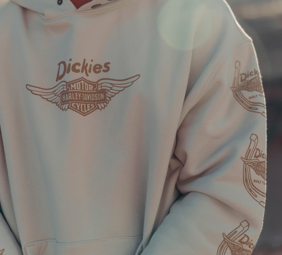 Felpa con cappuccio beige della collezione Dickies x Harley-Davidson. Logo frontale Dickies e scudo alato Harley-Davidson. Pattern ripetuto sulle maniche