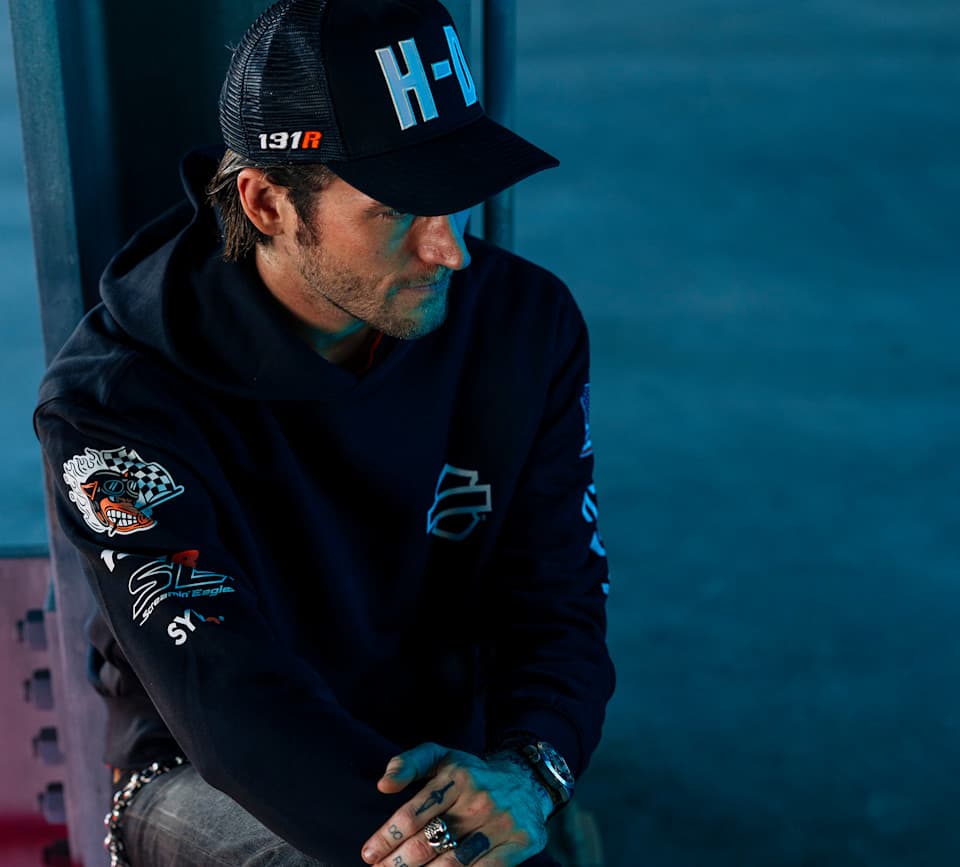 Uomo con cappellino nero H-D e felpa con cappuccio nera, dettagli Screamin' Eagle sulla manica. Abbigliamento ufficiale Harley-Davidson.
