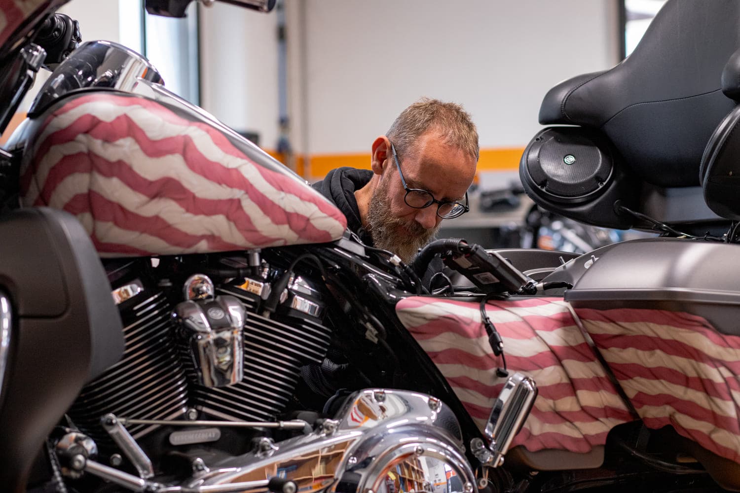 Manutenzione Harley-Davidson: cura e attenzione ai dettagli Tecnico specializzato Harley-Davidson esamina il motore di una moto custom con livrea a bandiera americana, in fase di manutenzione.