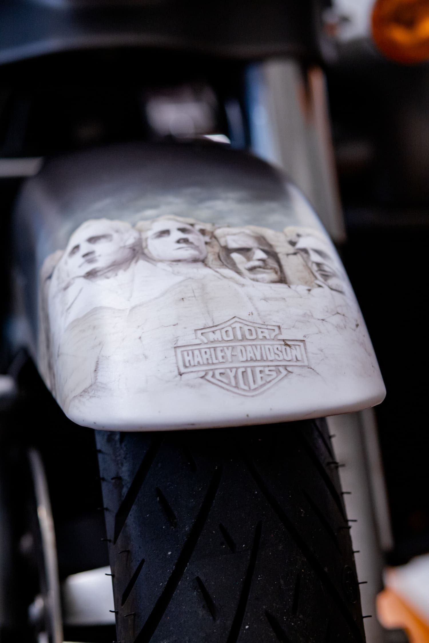 Dettaglio parafango custom Harley-Davidson Mount Rushmore. Parafango anteriore personalizzato di moto Harley-Davidson con scultura in rilievo ispirata al Monte Rushmore e logo. Visibile pneumatico.