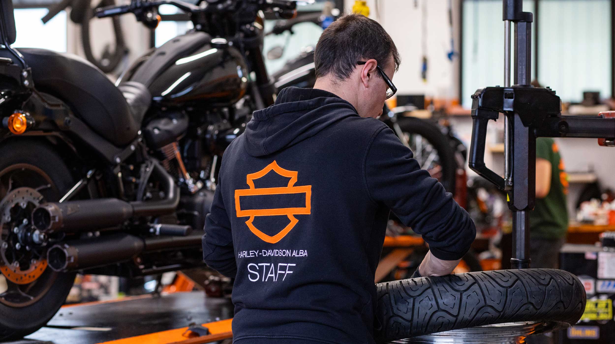 Manutenzione professionale Harley-Davidson ad Alba Tecnico Harley-Davidson Alba in officina, con abbigliamento staff, mentre esegue manutenzione su uno pneumatico moto.
