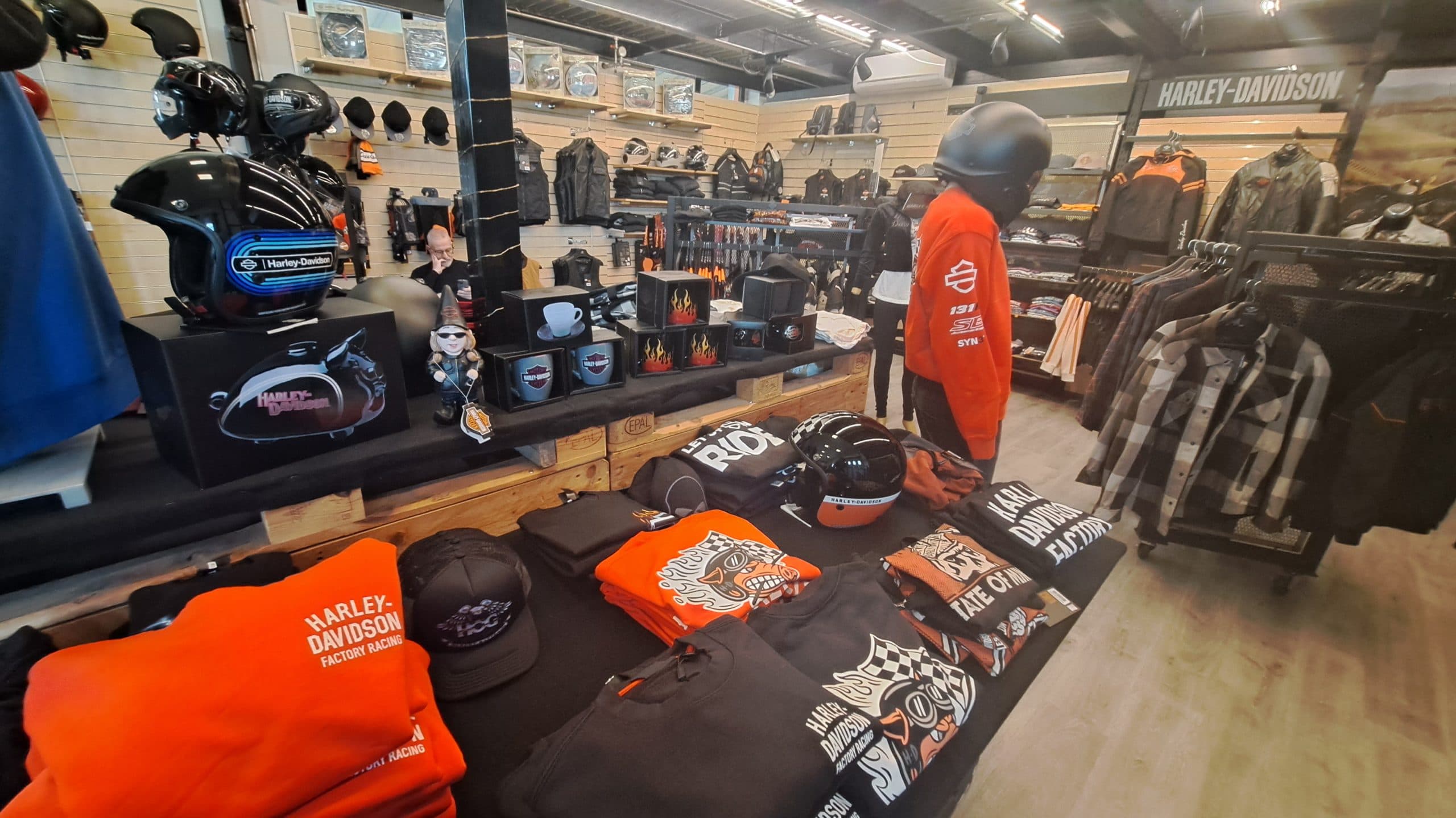 1000813332.jpg Area merchandising di concessionaria Harley-Davidson con abbigliamento, caschi e accessori. In evidenza felpe, magliette, cappellini e caschi da moto Harley-Davidson.