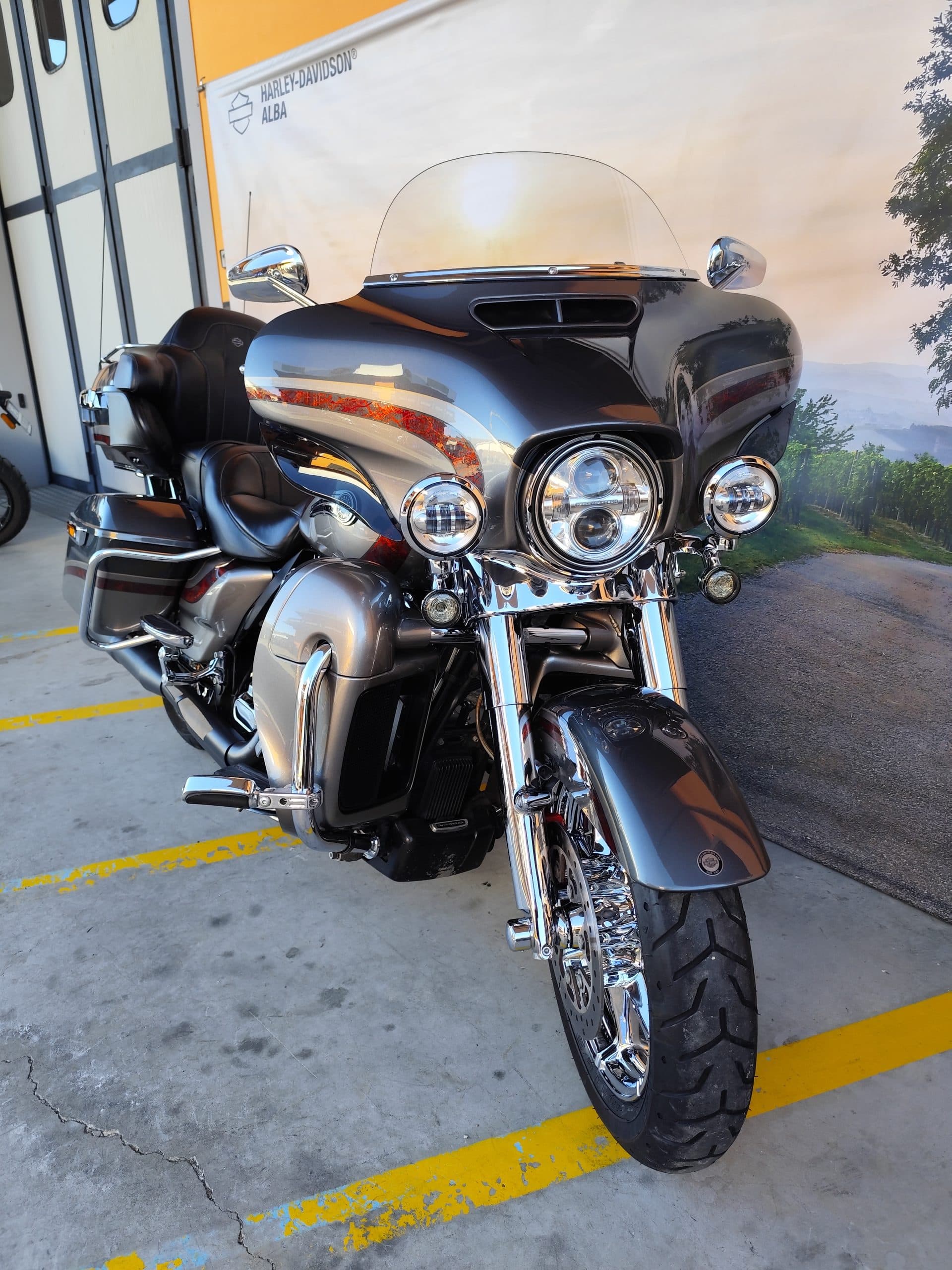 IMG_20260217_091344.jpg Harley-Davidson touring grigia con fari LED e cromature, esposta presso la concessionaria di Alba, su sfondo paesaggistico.