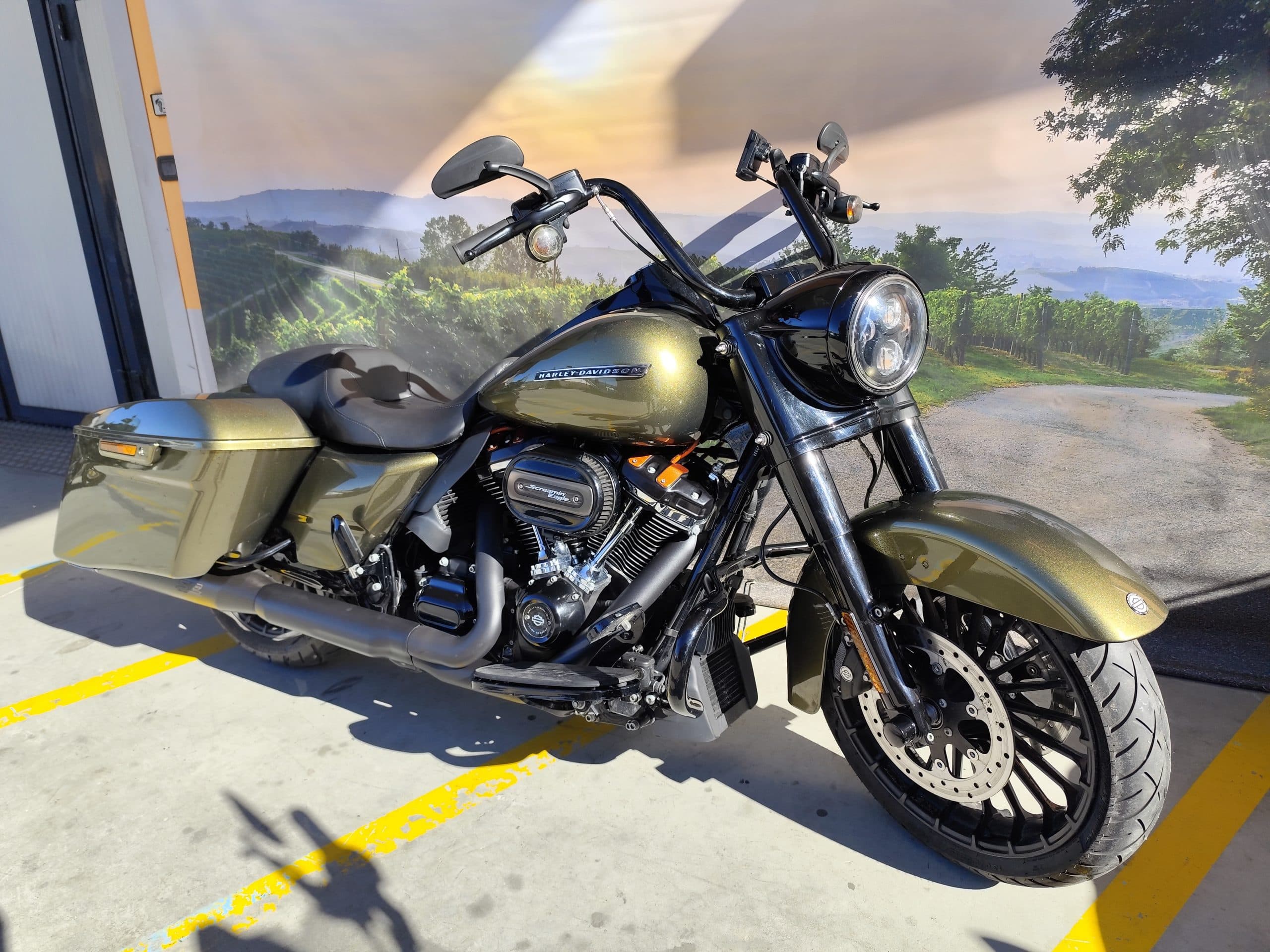 IMG_20260217_122053.jpg Harley-Davidson Road Glide Special colorazione Deadwood Green, con motore Milwaukee-Eight 114, scarico Screamin' Eagle e manubrio ape-hanger, parcheggiata su asfalto con strisce gialle, davanti a un fondale con paesaggio collinare e vigneti.