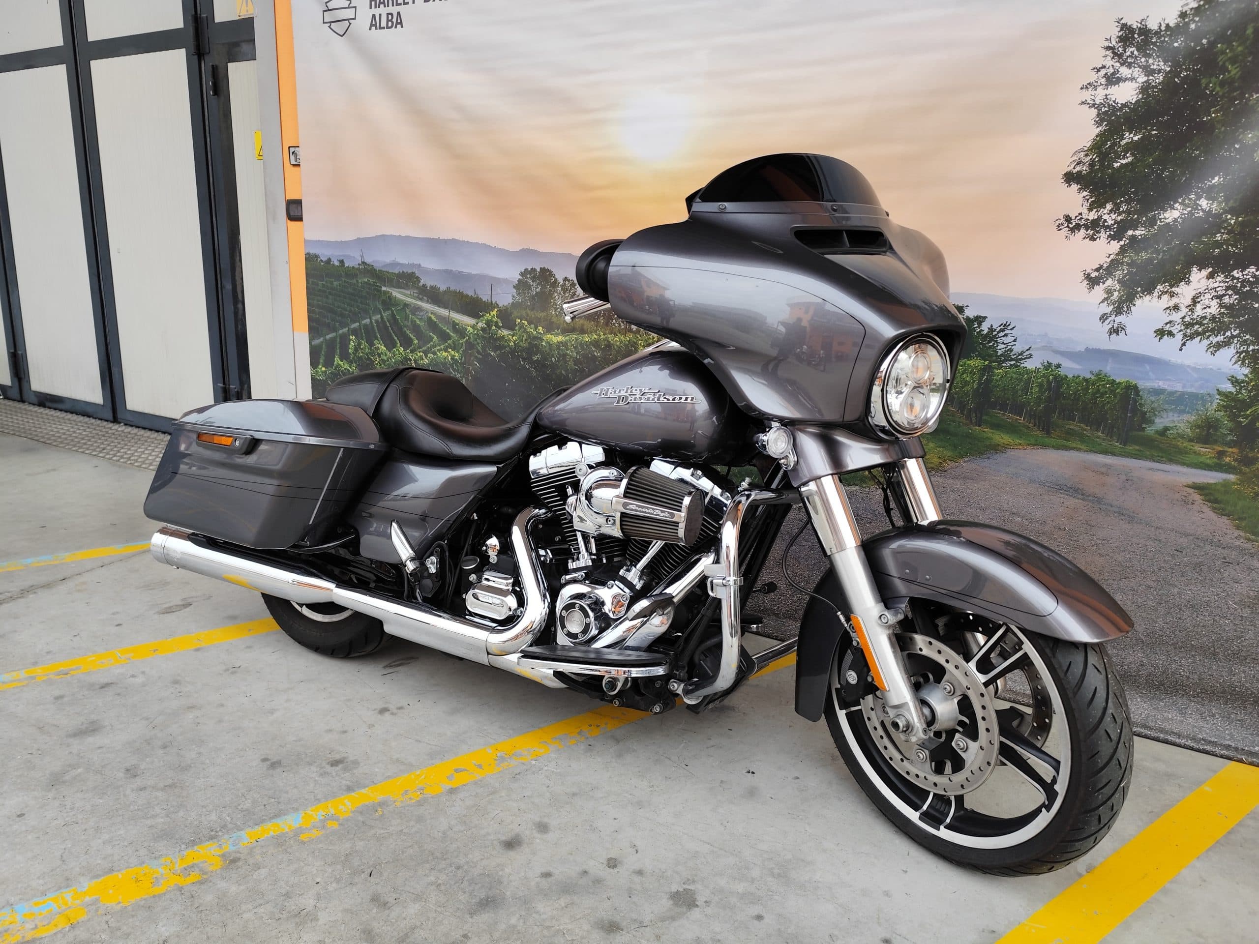 IMG_20260227_085436.jpg Harley-Davidson Street Glide grigia, con motore cromato e scarichi lucidi, esposta davanti al banner Harley-Davidson Alba.