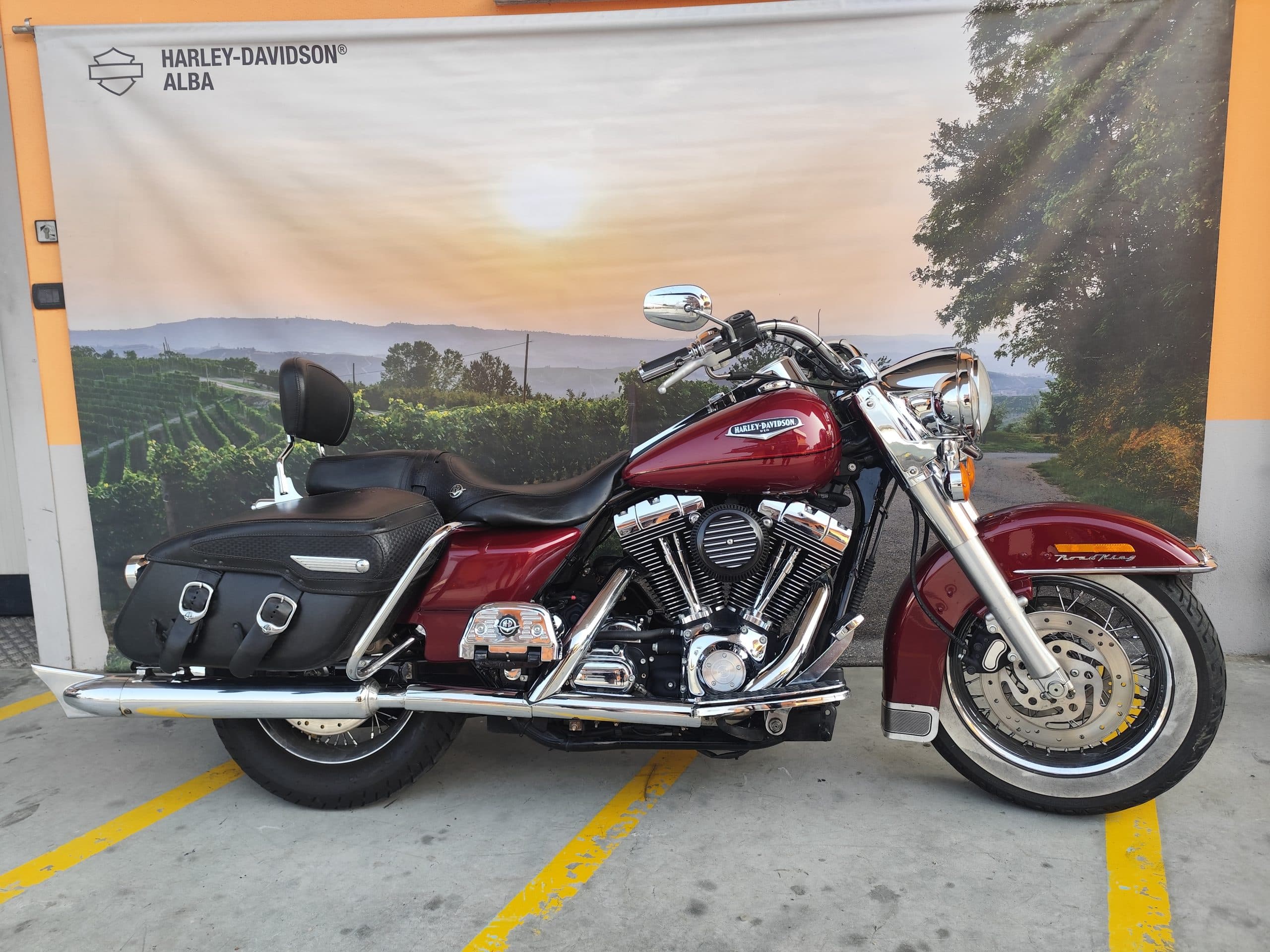 IMG_20260304_101935-scaled Harley-Davidson Road King rossa, con motore e scarichi cromati, esposta davanti al banner promozionale Harley-Davidson Alba.