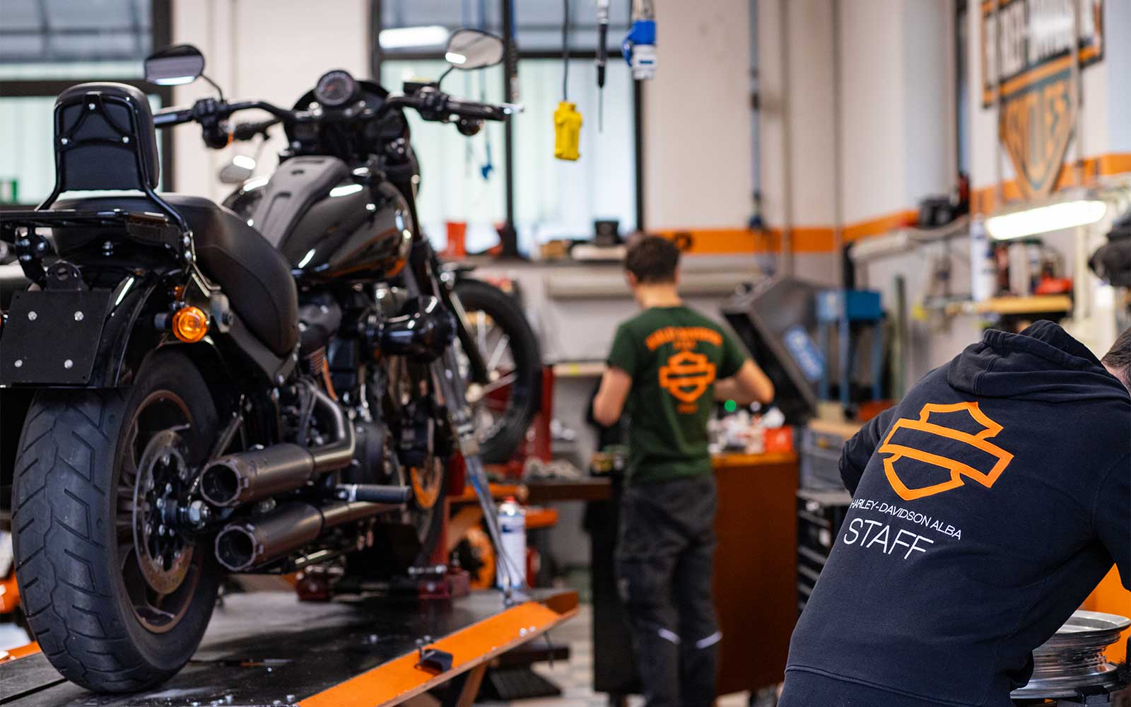 Servizio officina specializzato Harley-Davidson Officina Harley-Davidson Alba con moto in manutenzione su sollevatore e staff in abbigliamento brandizzato al lavoro.
