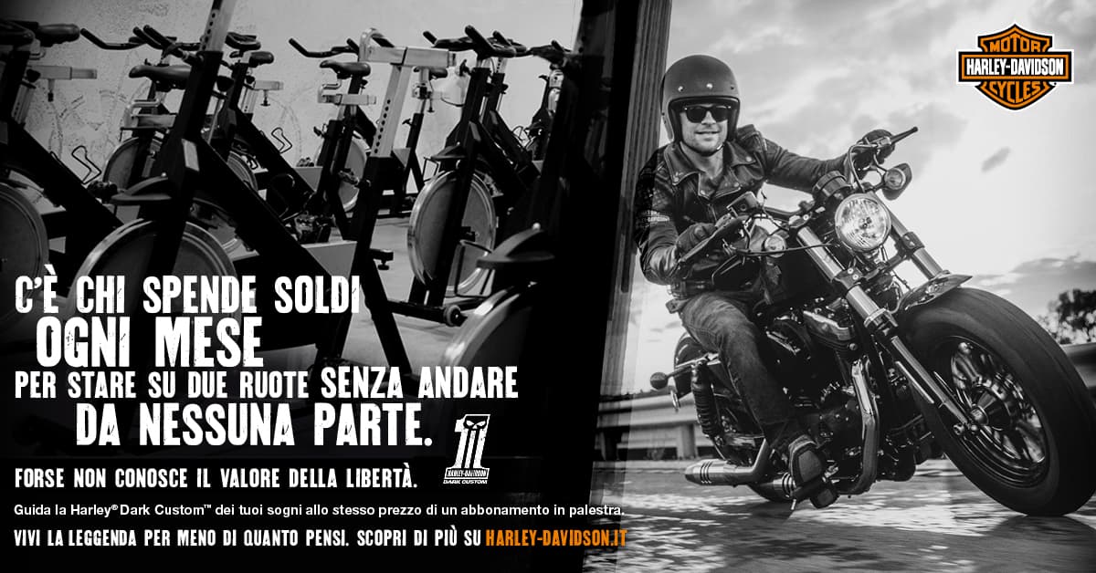 1464339046FB_1200x628_Affordability_Gym_FortyEight Pubblicità Harley-Davidson: un motociclista su Dark Custom in movimento, contrapposto a spin bike, celebra la libertà della moto.