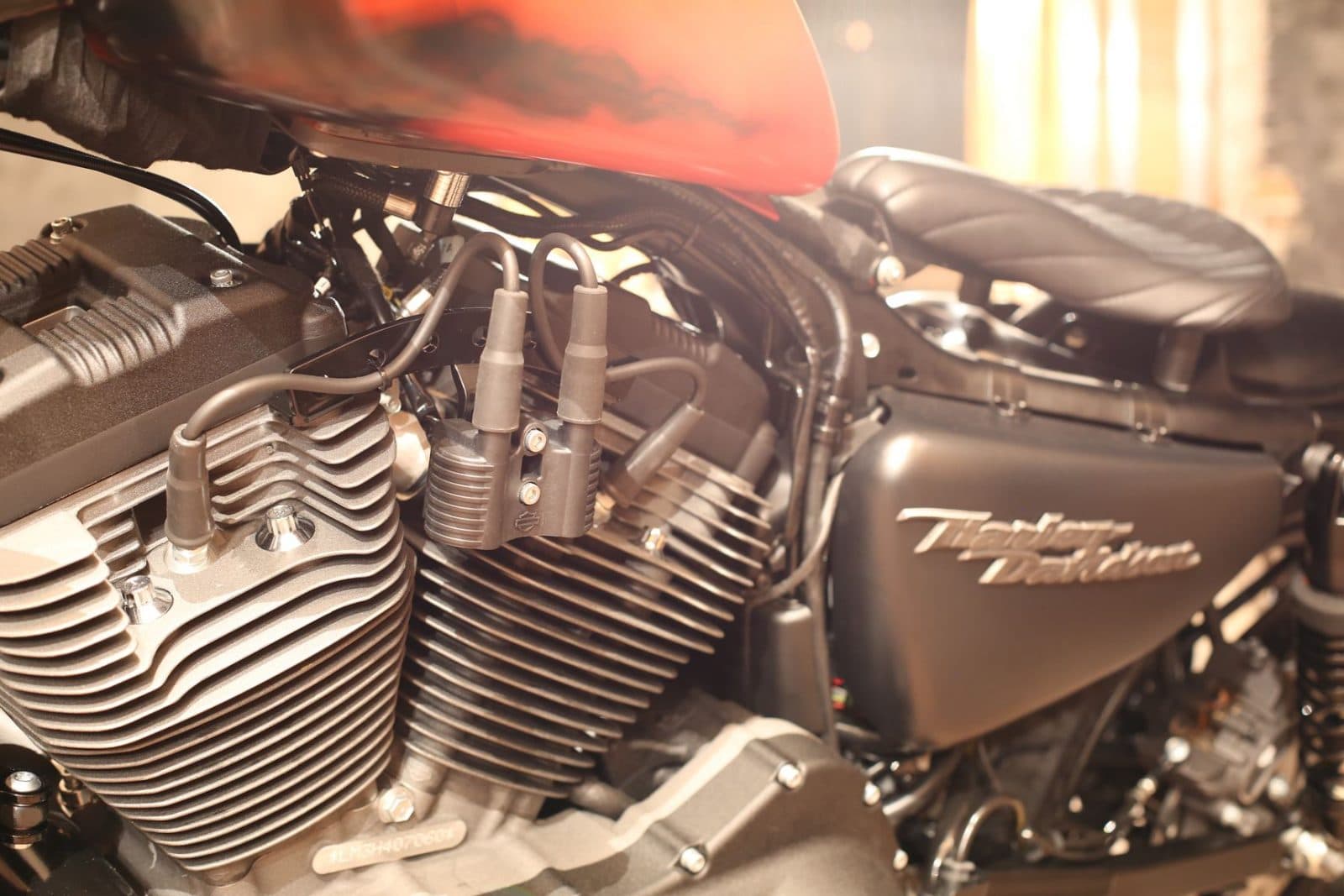 1484384923piccola3.jpg Primo piano del motore V-twin di una moto Harley-Davidson, con cilindri alettati, cavi candela e bobine. Logo Harley-Davidson sul carter.