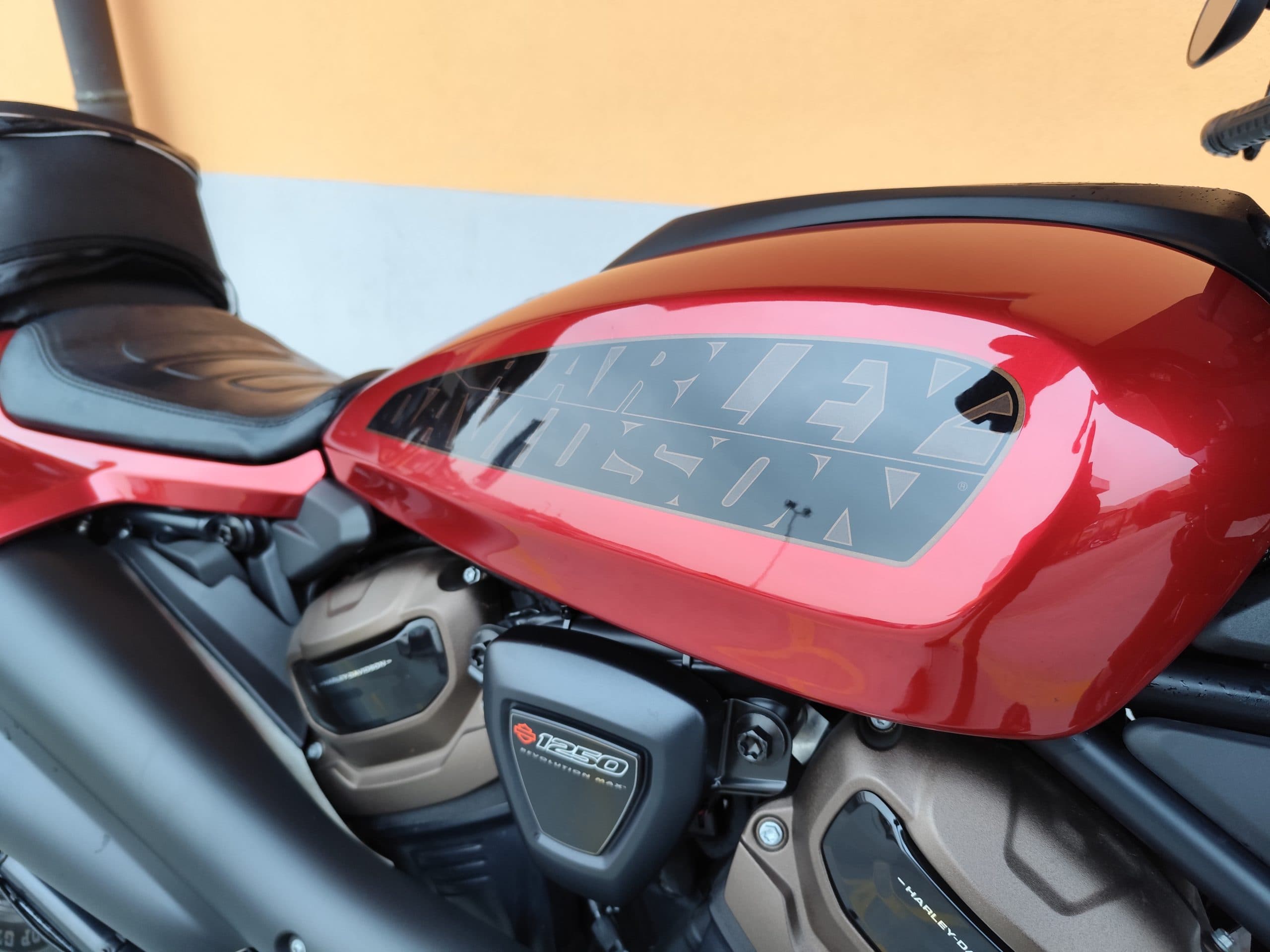 Harley-Davidson Revolution Max 1250: Dettaglio Serbatoio Primo piano del serbatoio rosso lucido di una moto Harley-Davidson, con logo stilizzato nero e dettagli del motore Revolution Max 1250.