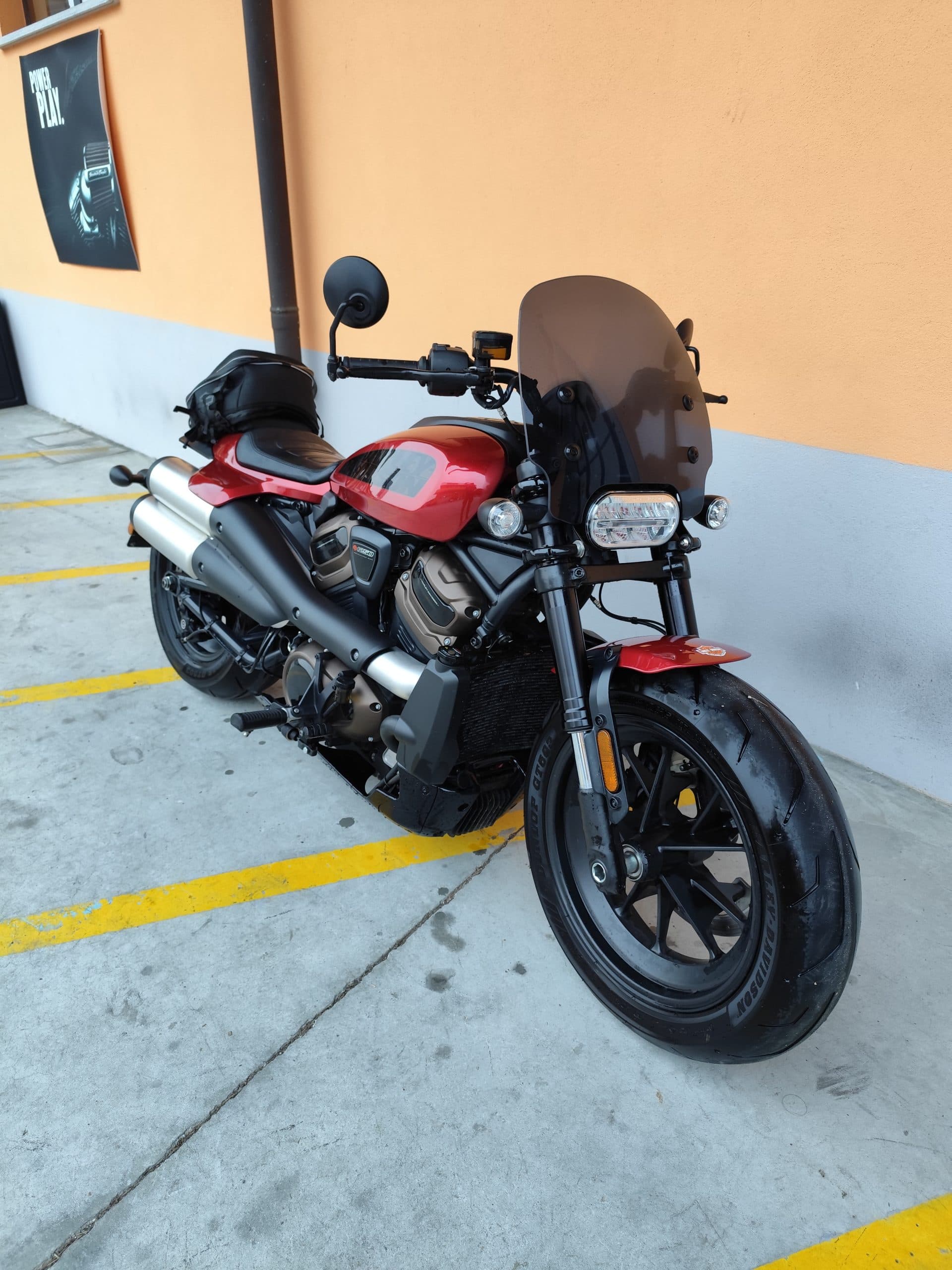 Nuova Harley-Davidson Sportster S rossa: scopri la moto Harley-Davidson Sportster S rossa con parabrezza fumé, scarichi doppi e motore bronzo, parcheggiata su asfalto.