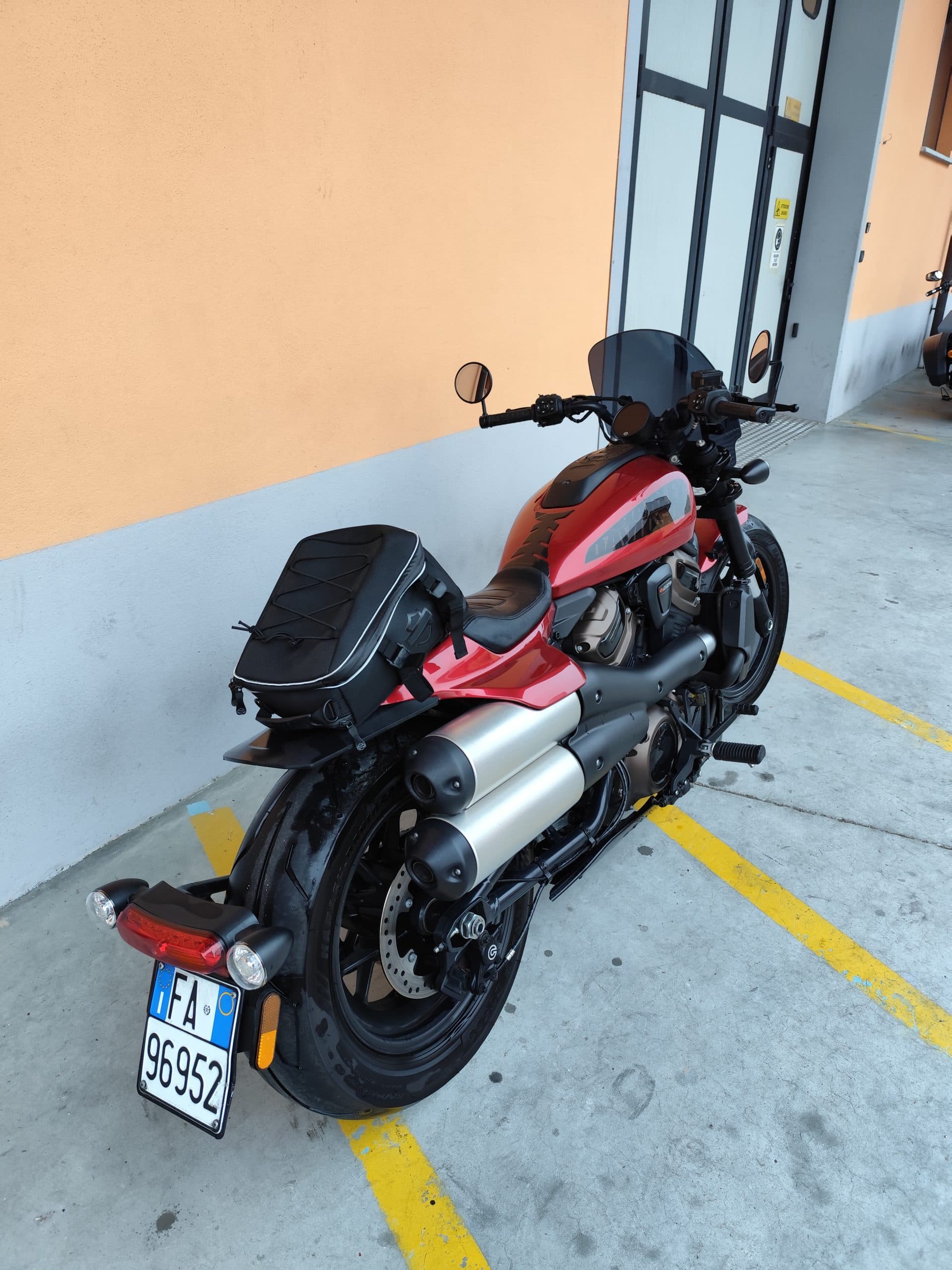Harley-Davidson Sportster S: design e accessori. Harley-Davidson Sportster S rossa, equipaggiata con borsa sella posteriore e cupolino, parcheggiata su pavimentazione in cemento.