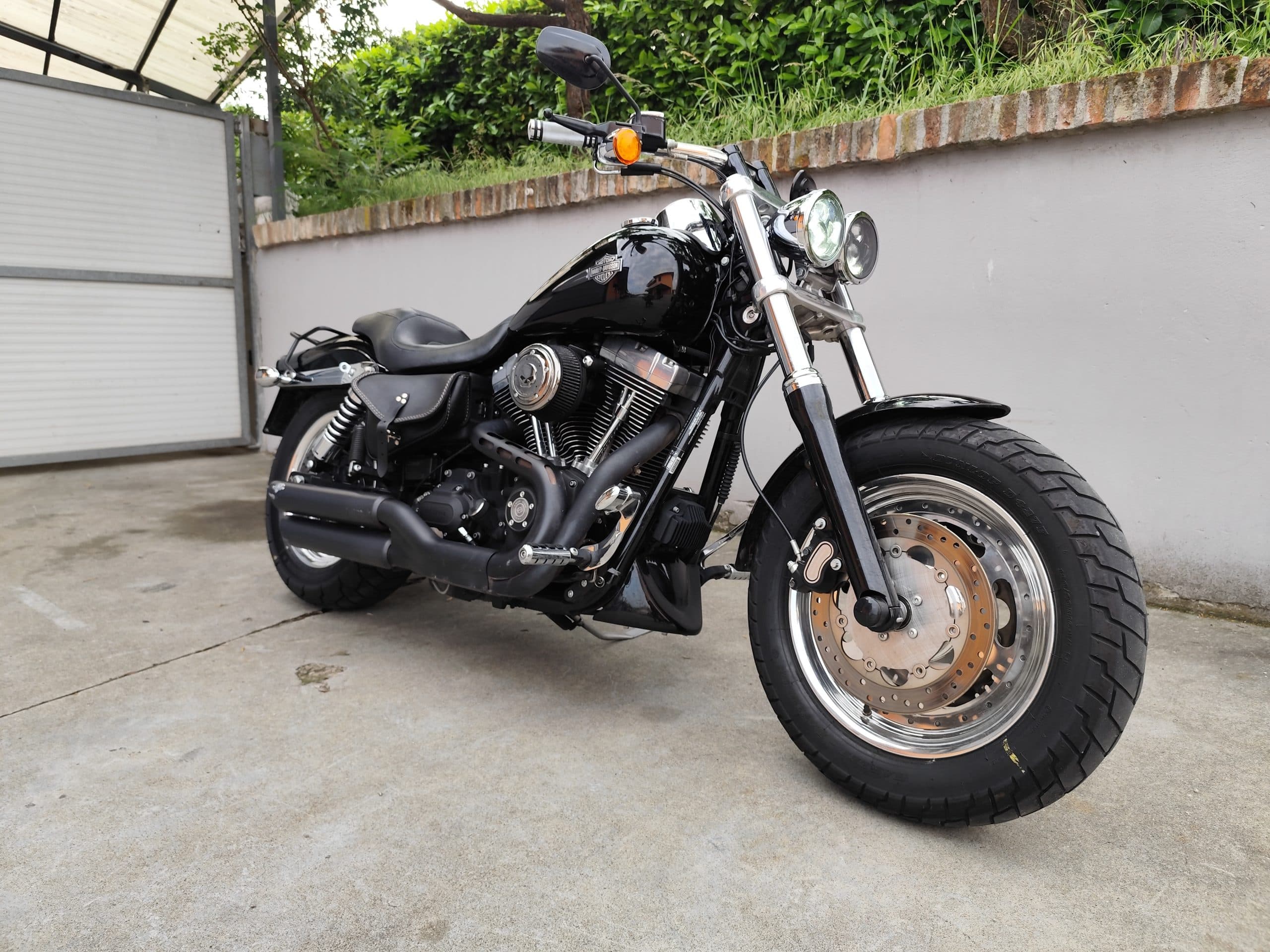 1749819270653.jpg Harley-Davidson Dyna Fat Bob nera, parcheggiata all'aperto, con dettagli del motore, scarichi neri e doppio faro anteriore. Ideale per test ride.