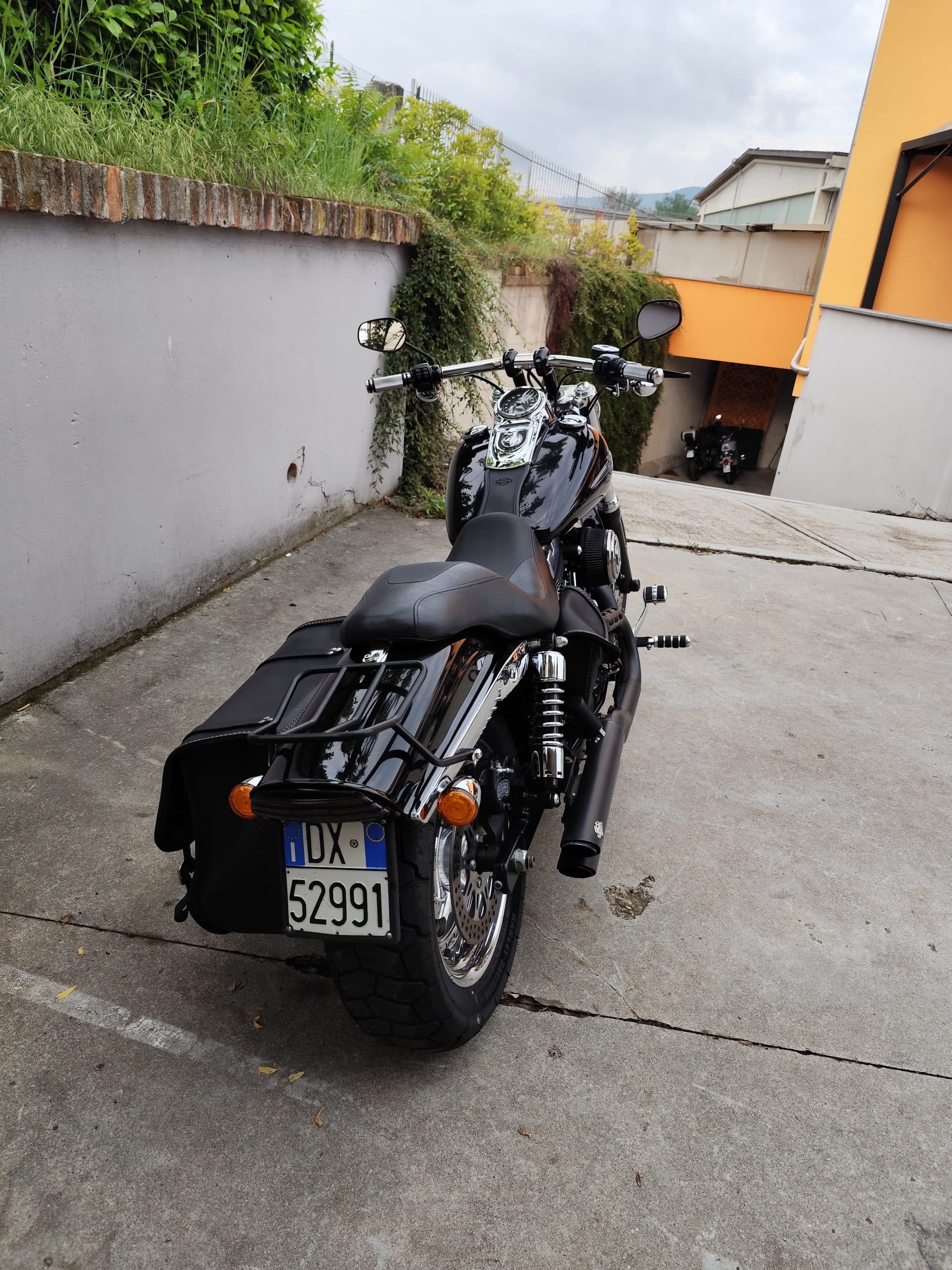 1749819270802.jpg Harley-Davidson nera, vista posteriore destra, con borse laterali, portapacchi e scarico custom. Dettagli cromati e targa italiana DX 52991. Ideale per gli appassionati di moto e motori.