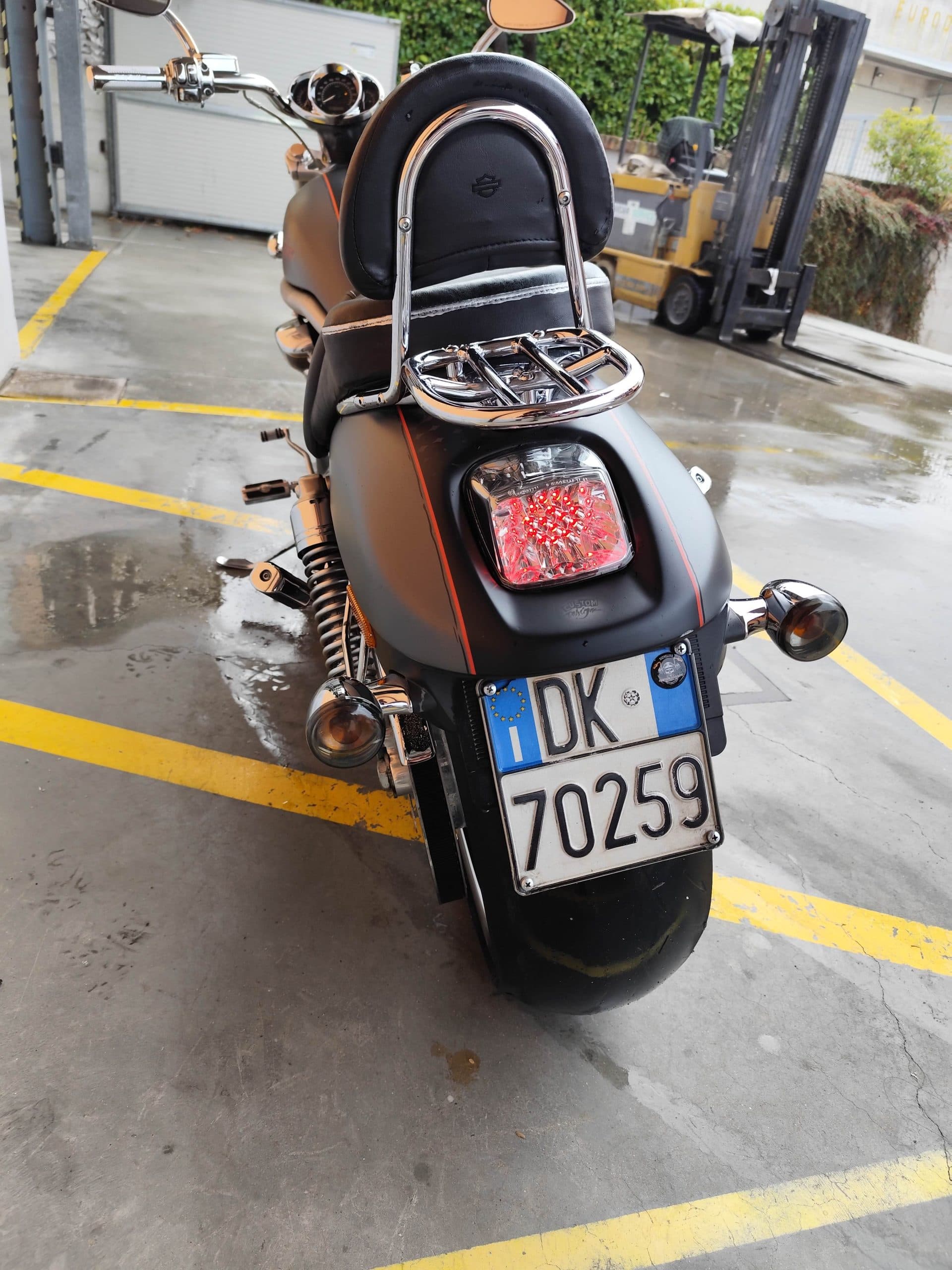 1766134081981.jpg Moto Harley-Davidson con finitura nero opaco e strisce arancioni, vista posteriore. Dettagli: schienalino, portapacchi cromato, fanale LED, targa italiana DK 70259.