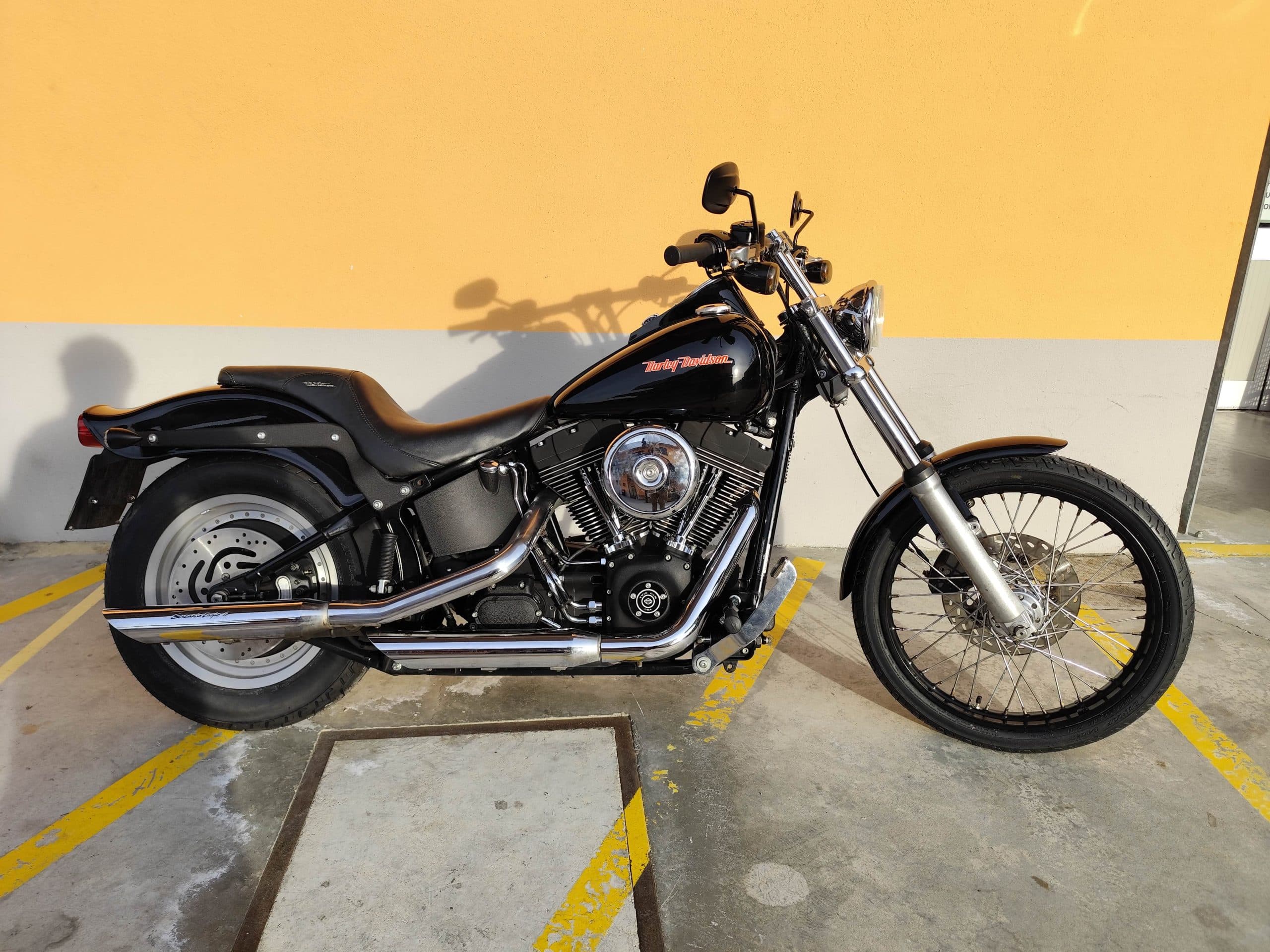 1768227369940.jpg Harley-Davidson nera, modello cruiser, parcheggiata. Dettagli del motore V-twin, scarichi cromati e ruote a raggi. Perfetta per gli amanti dei motori.
