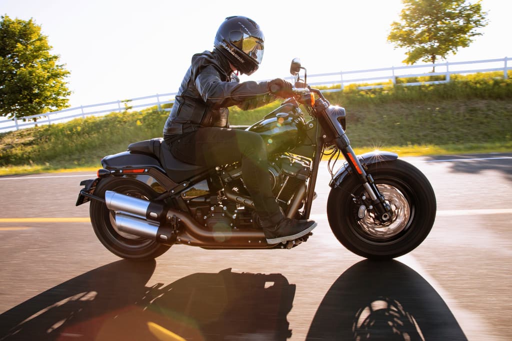 201461_my21_fxfbs_hdi_riding_0203_jk.jpg Motociclista con abbigliamento tecnico e casco integrale su Harley-Davidson in corsa su strada, con sole e lunghe ombre. Ideale per test ride.