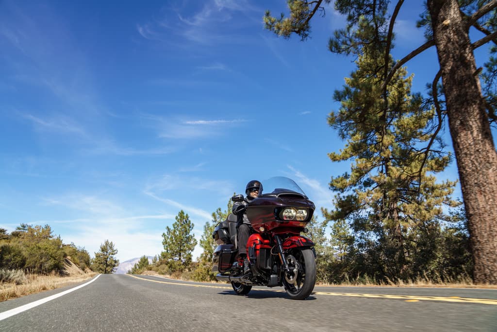210249_my22_fltrkse_cvo_road_glide_limited_riding_sgt_0258 Harley-Davidson Road Glide rossa in movimento su strada panoramica, pilota con casco. Cielo azzurro e alberi. Perfetta per test ride.