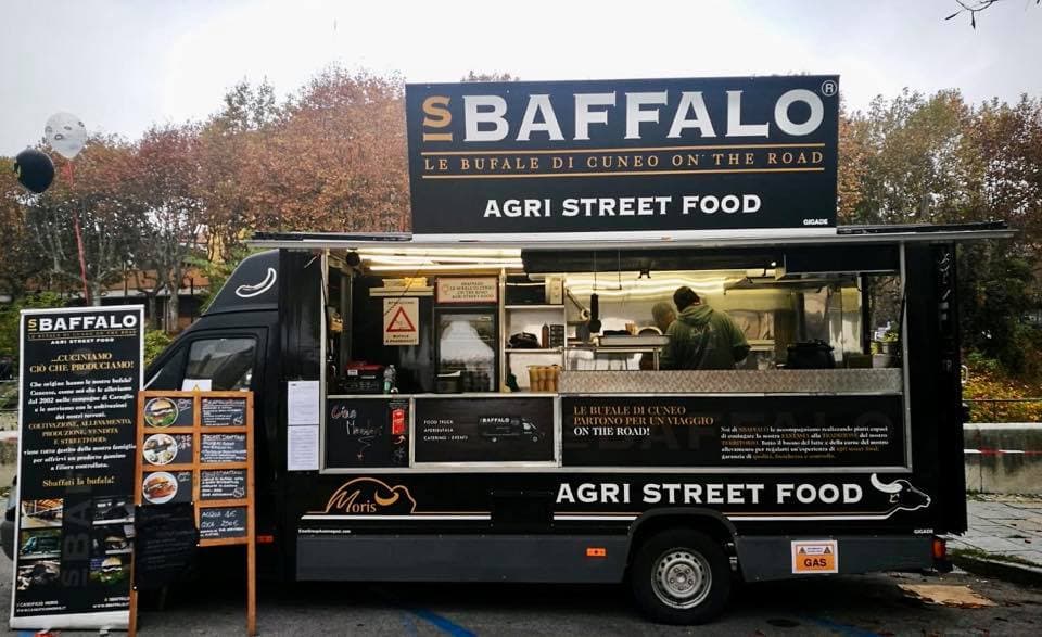 FB_OPENDAY4.jpg Food truck nero SBAFFALO AGRI STREET FOOD con insegna luminosa e menù esposto, operatore a bordo, in un evento all'aperto con alberi aut