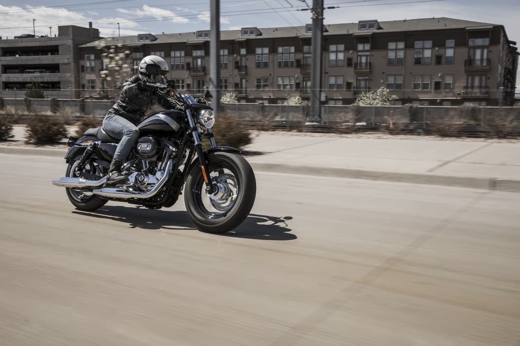 Model Year 2019 GAP Photography. INTERNATIONAL ONLY Motociclista con abbigliamento tecnico in test ride su Harley-Davidson nera su strada urbana, edifici sullo sfondo.