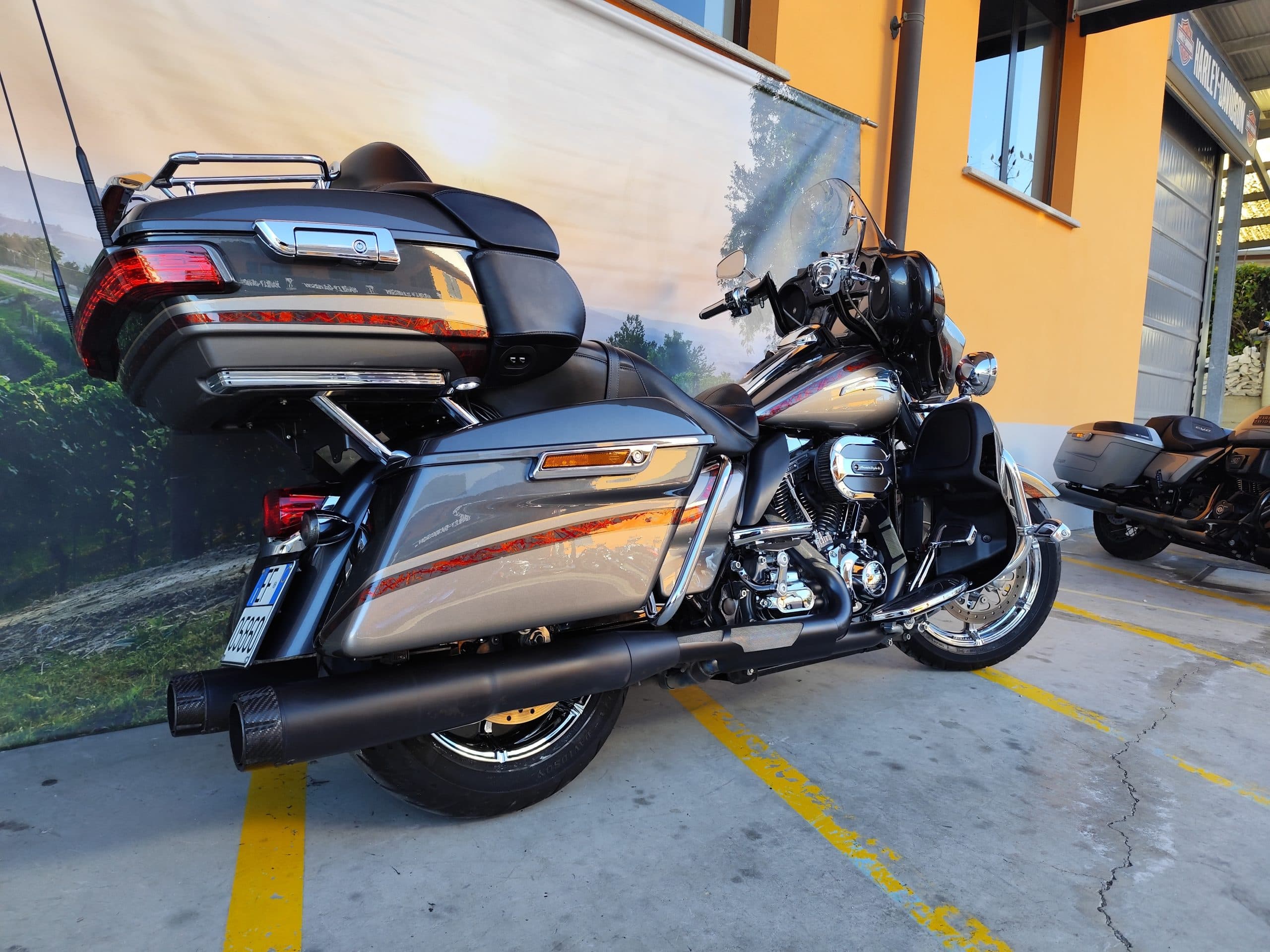 IMG_20260217_091359.jpg Harley-Davidson touring grigia con finiture cromate e dettagli rossi, parcheggiata davanti a una concessionaria. Evidenti motore, scarichi neri e bor
