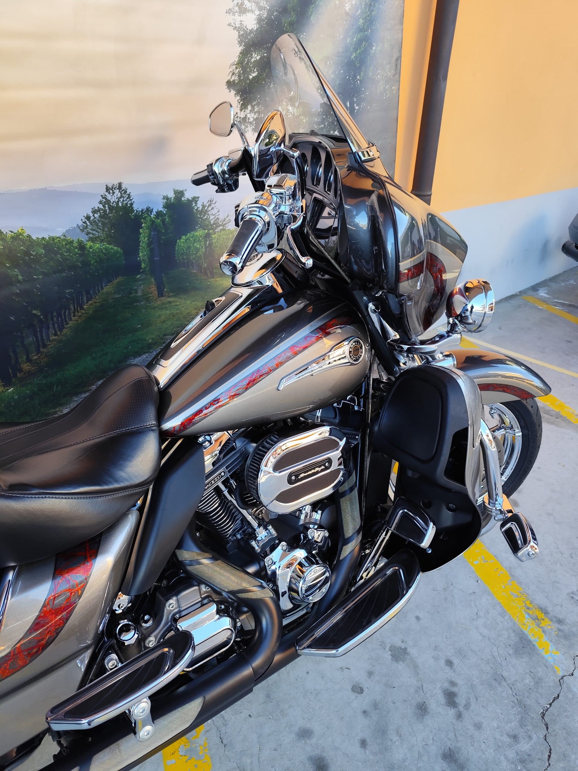 IMG_20260217_091406.jpg Harley-Davidson touring con carenatura, parabrezza, motore V-twin cromato, finitura grigio metallizzato e grafiche rosse, su sfondo vigneto.