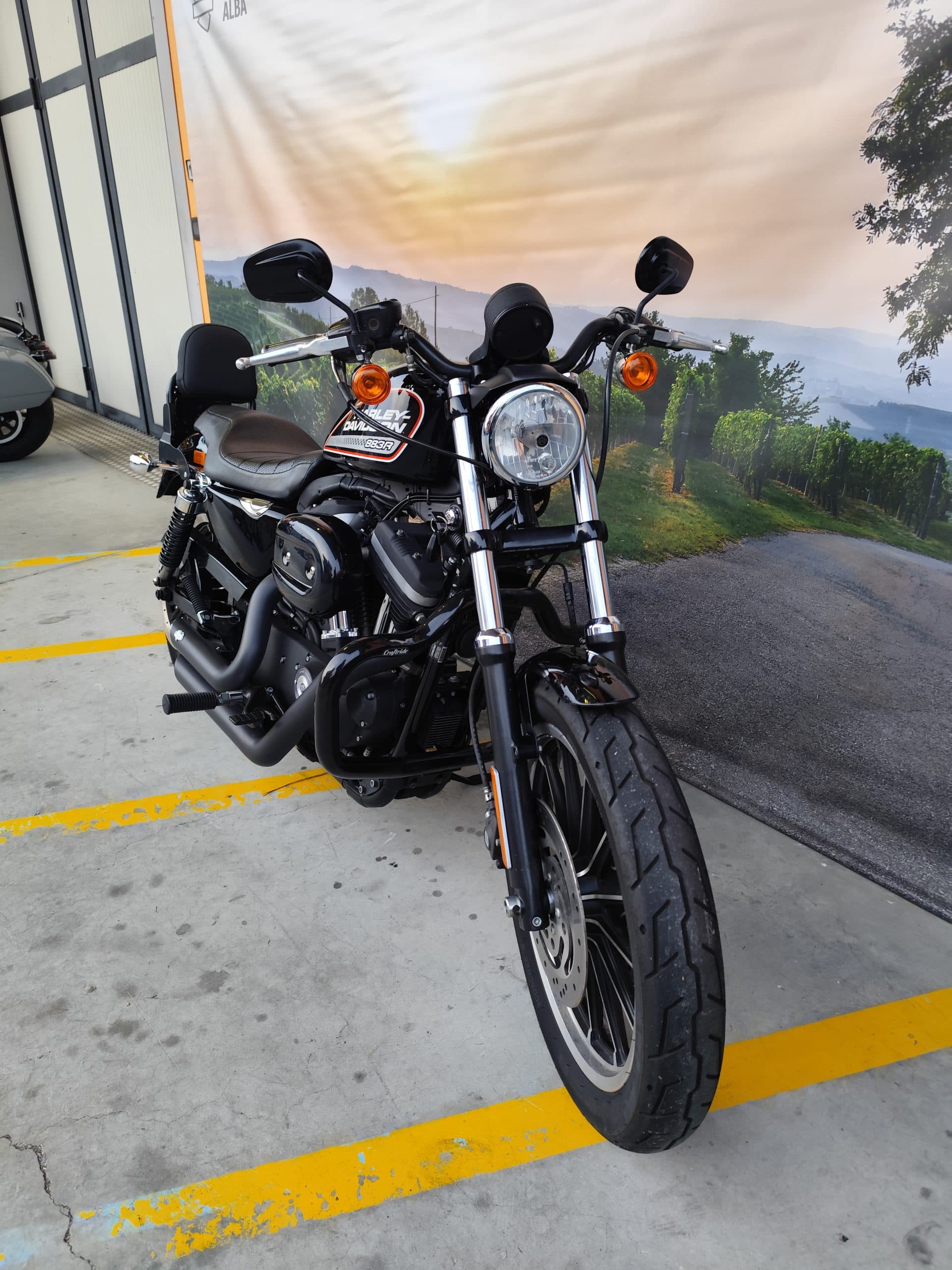 IMG_20260303_180117.jpg Harley-Davidson Sportster 883R nera su pavimentazione in cemento. Sfondo paesaggio collinare con vigneti. Pronta per test ride.
