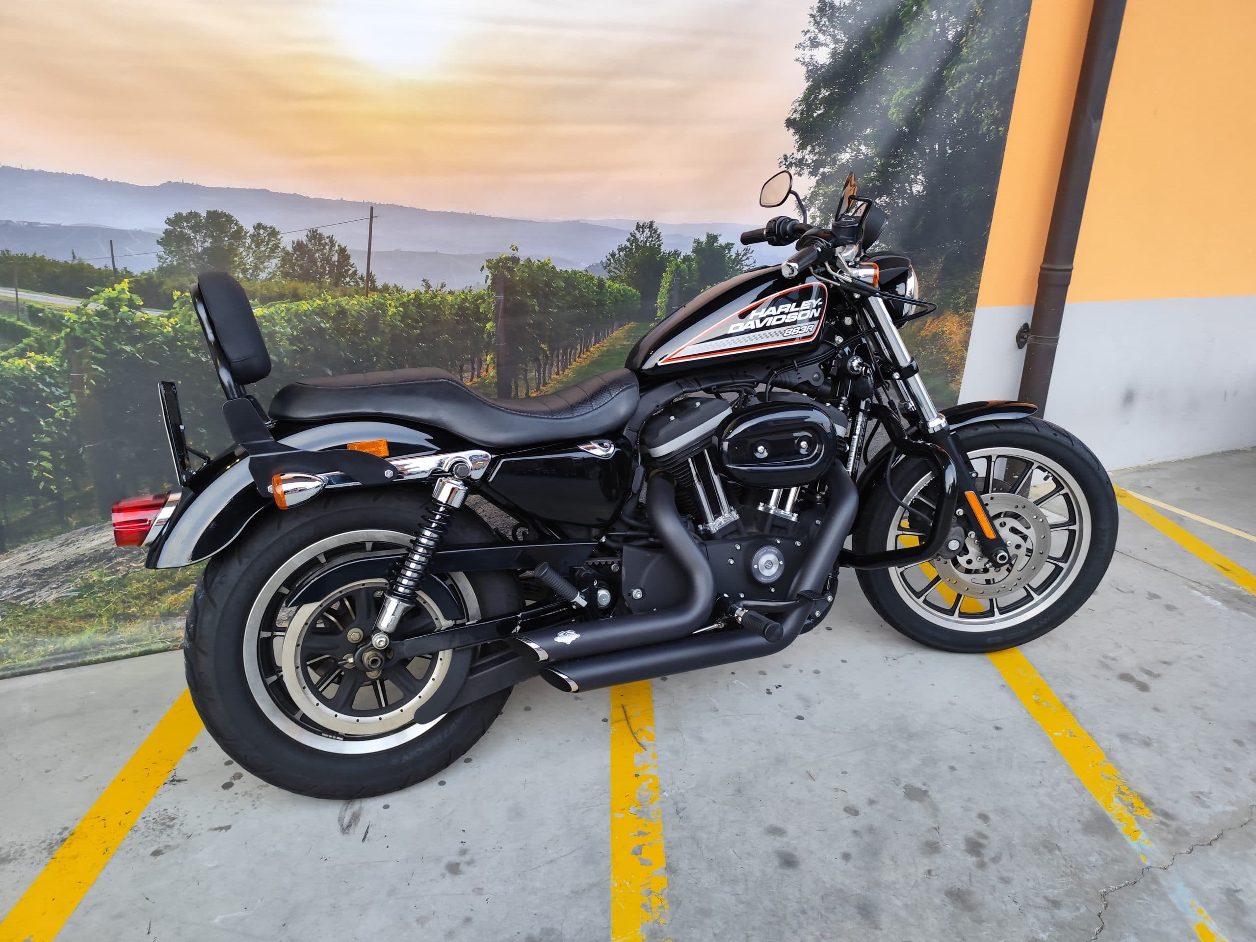 IMG_20260303_180121.jpg Harley-Davidson 883R nera parcheggiata in showroom con sfondo paesaggistico di vigneti e colline al tramonto, pronta per test ride.