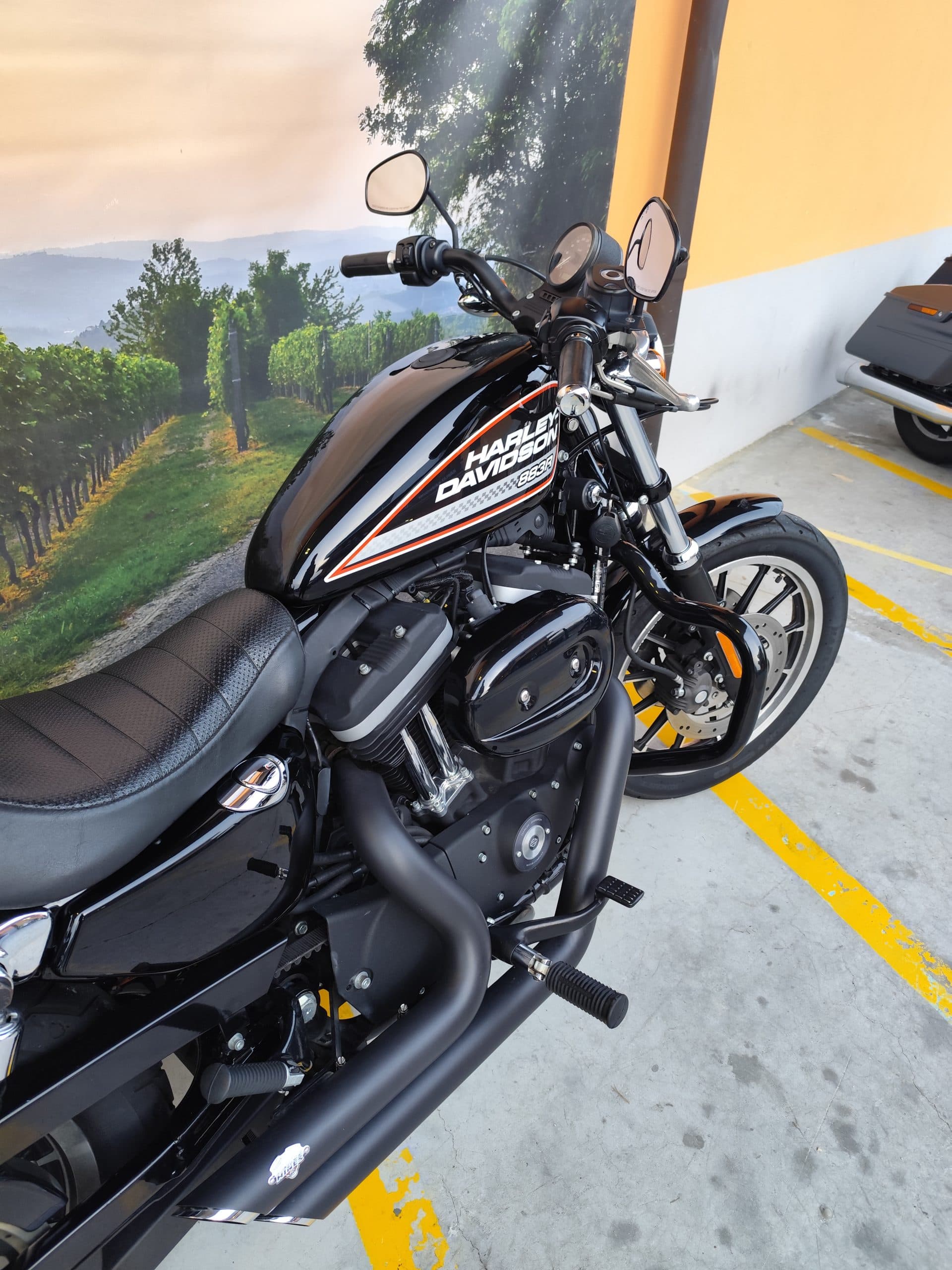 IMG_20260303_180127.jpg Harley-Davidson 883R nera, dettagli arancioni/bianchi, motore e scarichi neri. Moto esposta in concessionaria, disponibile per test ride.