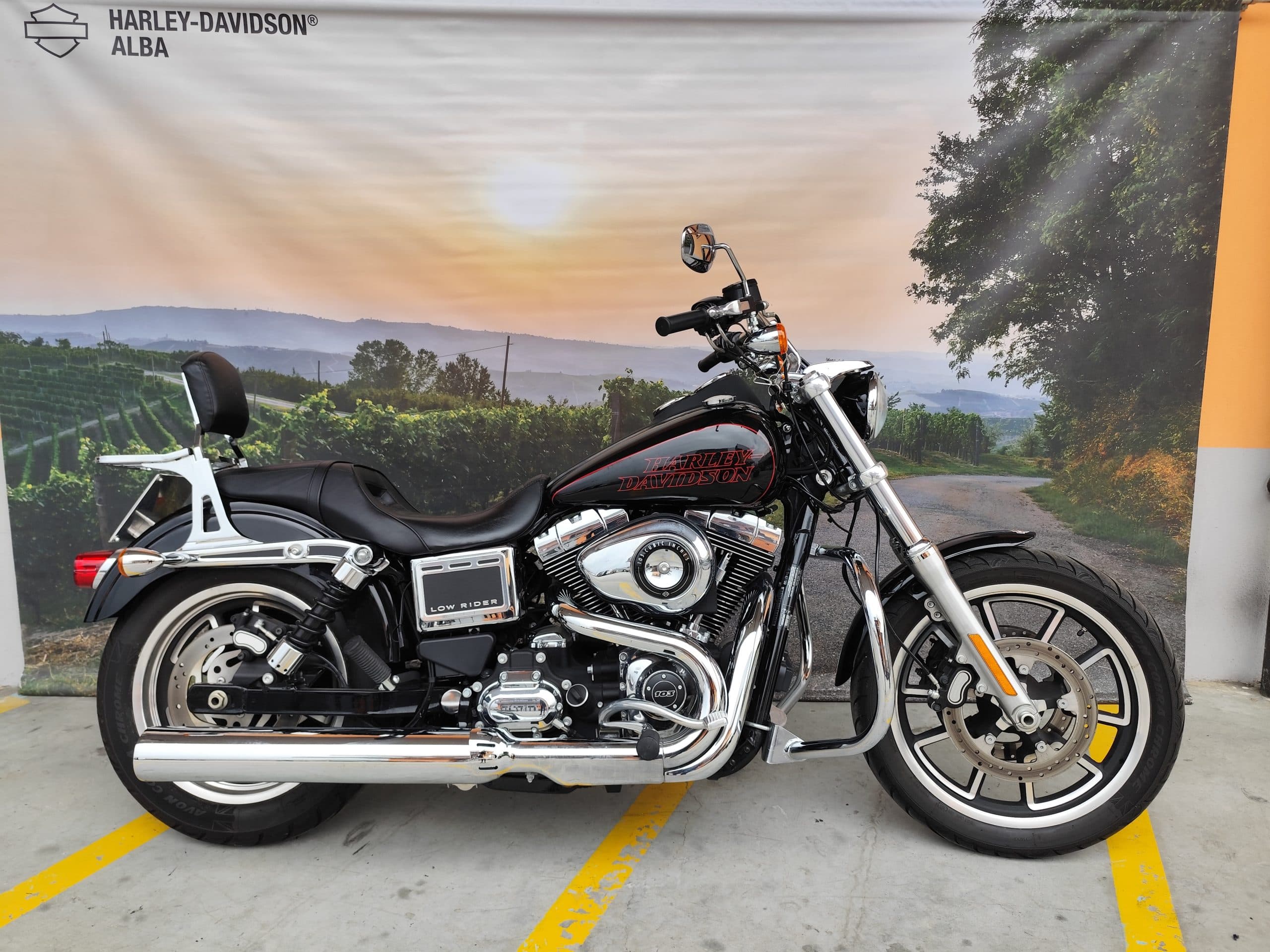 IMG_20260310_151553.jpg Harley-Davidson Low Rider nera, motore 103 cubic inches, con finiture cromate, esposta da Harley-Davidson Alba. Sfondo vigneti al tramonto.