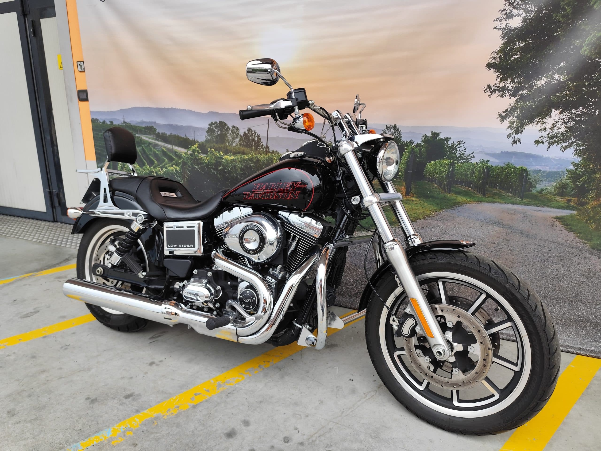IMG_20260310_151556.jpg Harley-Davidson Low Rider nera, motore 103 cubic inches, parcheggiata davanti a un fondale con vigneti e paesaggio collinare. Pronta per un test ride.