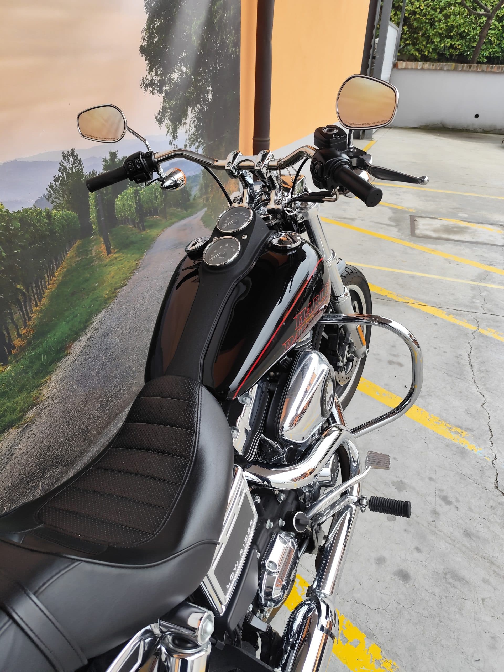 IMG_20260310_151616.jpg Harley-Davidson Low Rider nera con cromature, serbatoio con logo e pinstripes rossi. Sfondo paesaggistico. Pronta per un test ride.