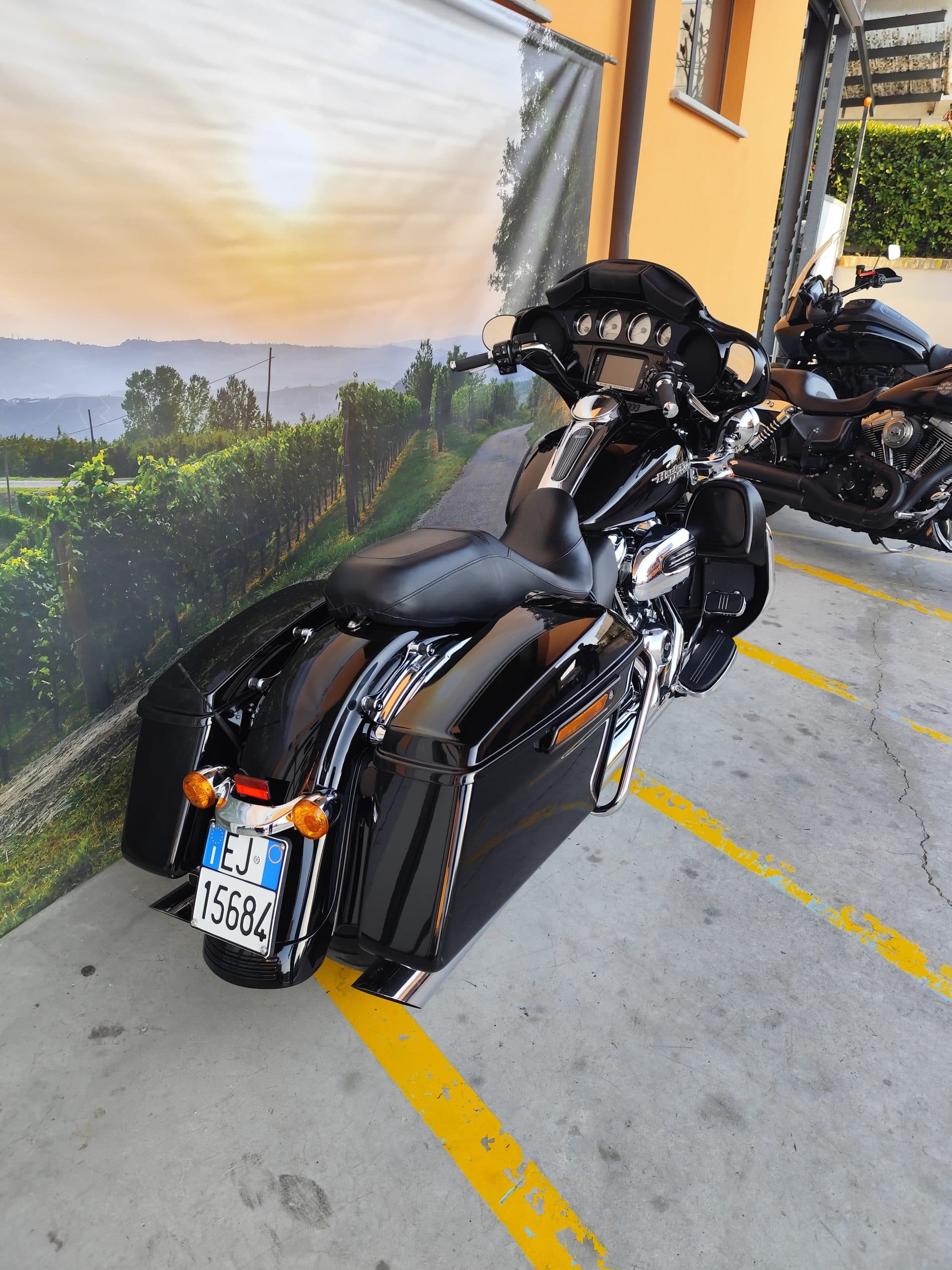 IMG_20260312_165835.jpg Harley-Davidson touring nera con targa EJ 15684 e altra moto, parcheggiate. Sfondo con vigneti e tramonto, ideale per un test ride.
