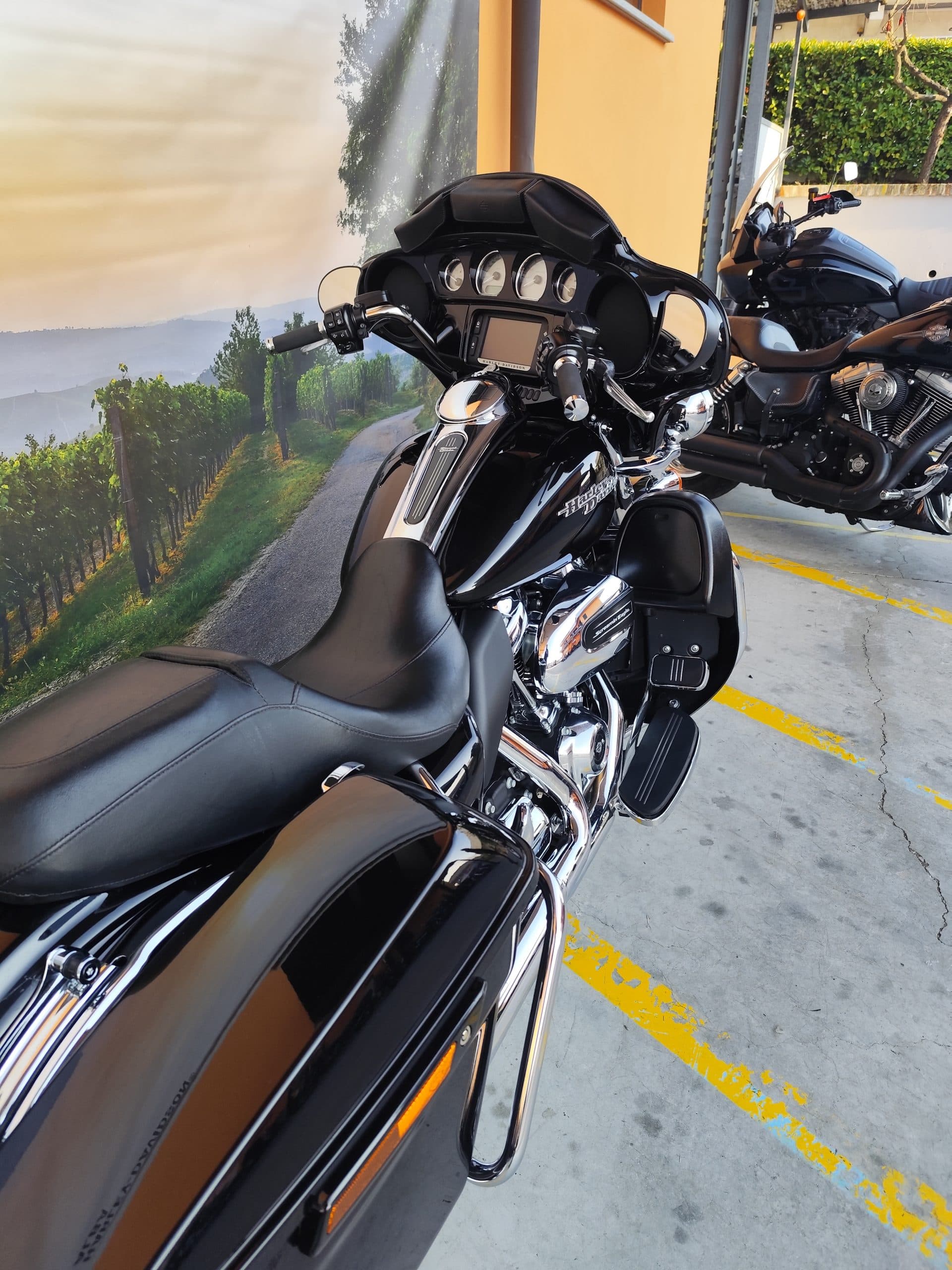 IMG_20260312_165838.jpg Harley-Davidson touring nera lucida con carenatura e borse laterali, dettagli cromati, esposta in concessionaria con murale di vigneti.