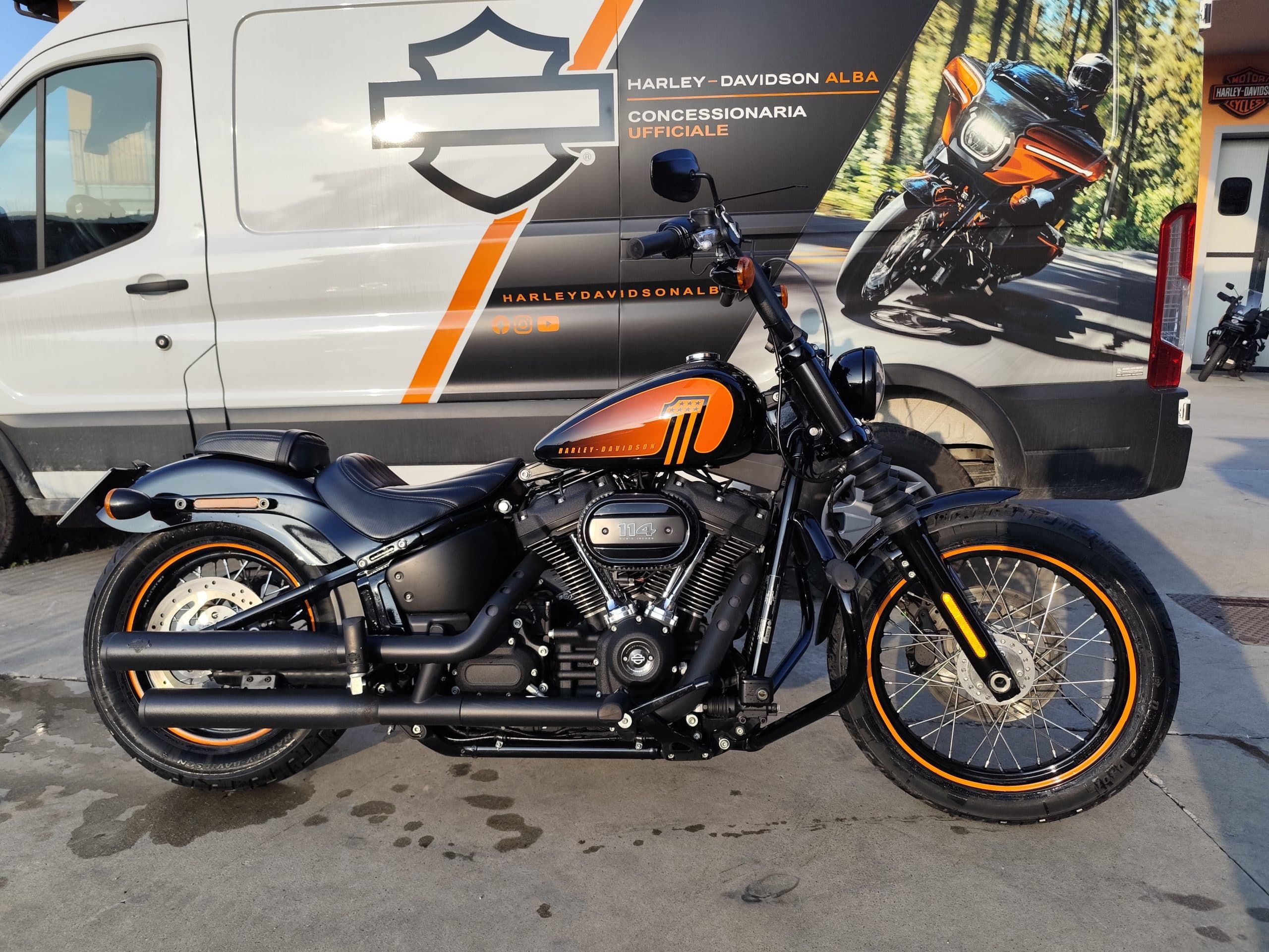 IMG_20260312_171304-1-scaled Moto Harley-Davidson nera e arancione, motore 114, esposta davanti al furgone della concessionaria ufficiale Harley-Davidson Alba.