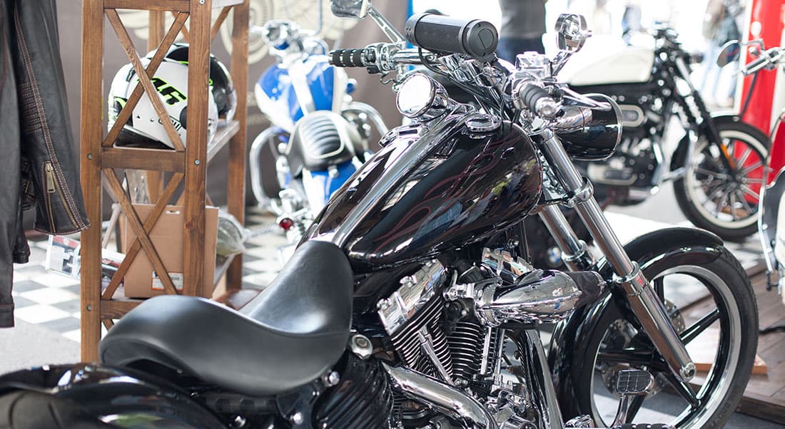 Il-salone-del-ciclo-e-motociclo Moto custom Harley-Davidson nera lucida con dettagli cromati e fiamme sul serbatoio, esposta con altri modelli e abbigliamento.